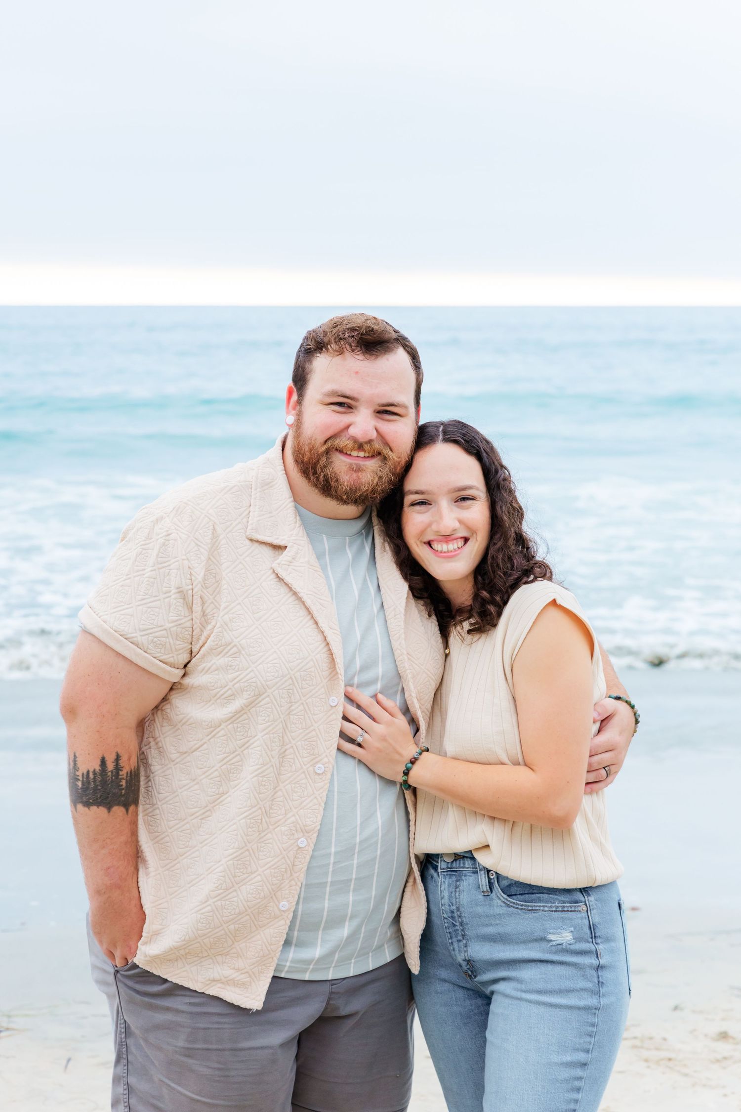 A couple shares an intimate moment while posing on a beautiful beach with waves behind them.