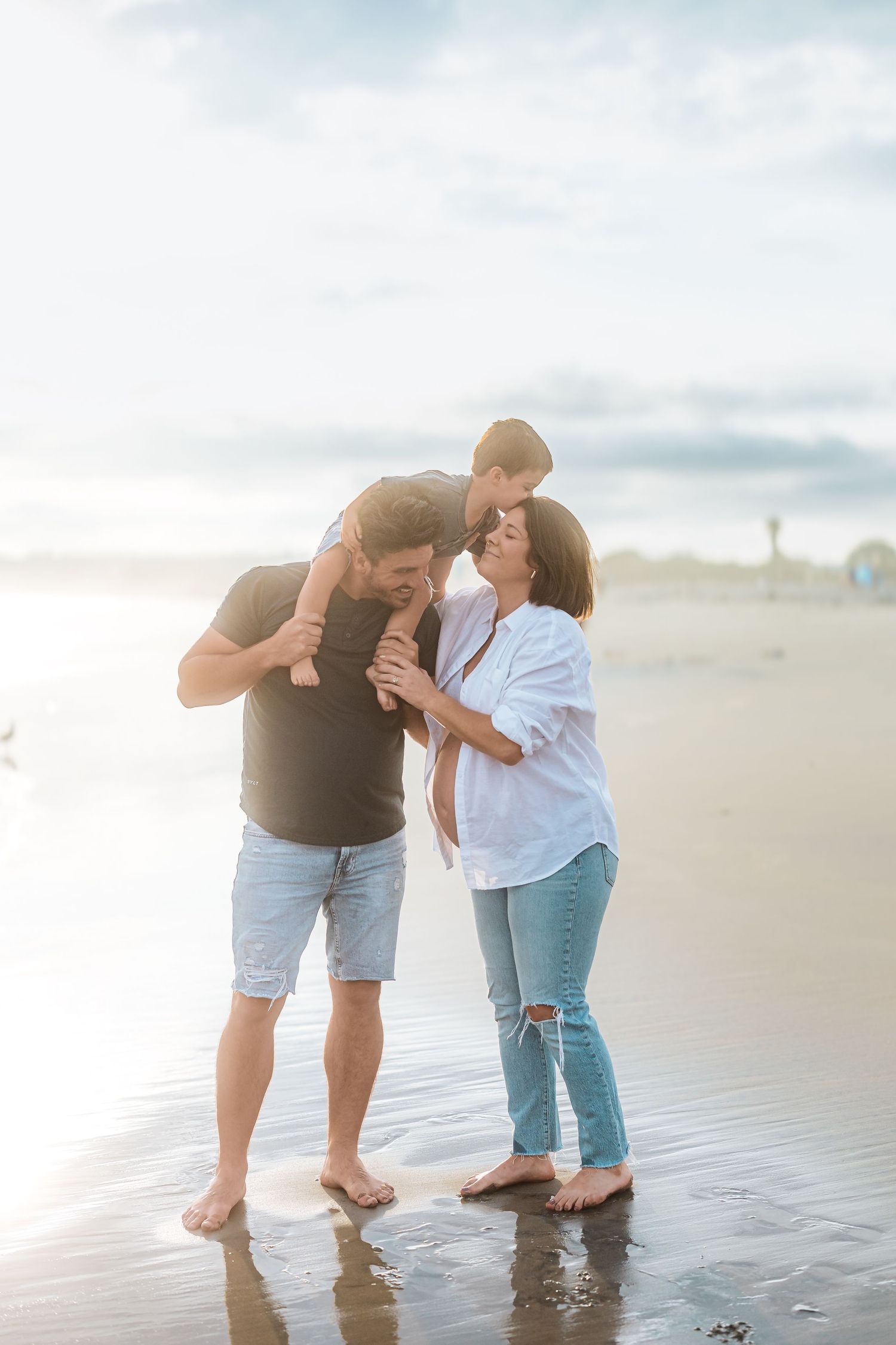 Expecting couple plays in the shallow ocean water during sunset maternity photoshoot.
