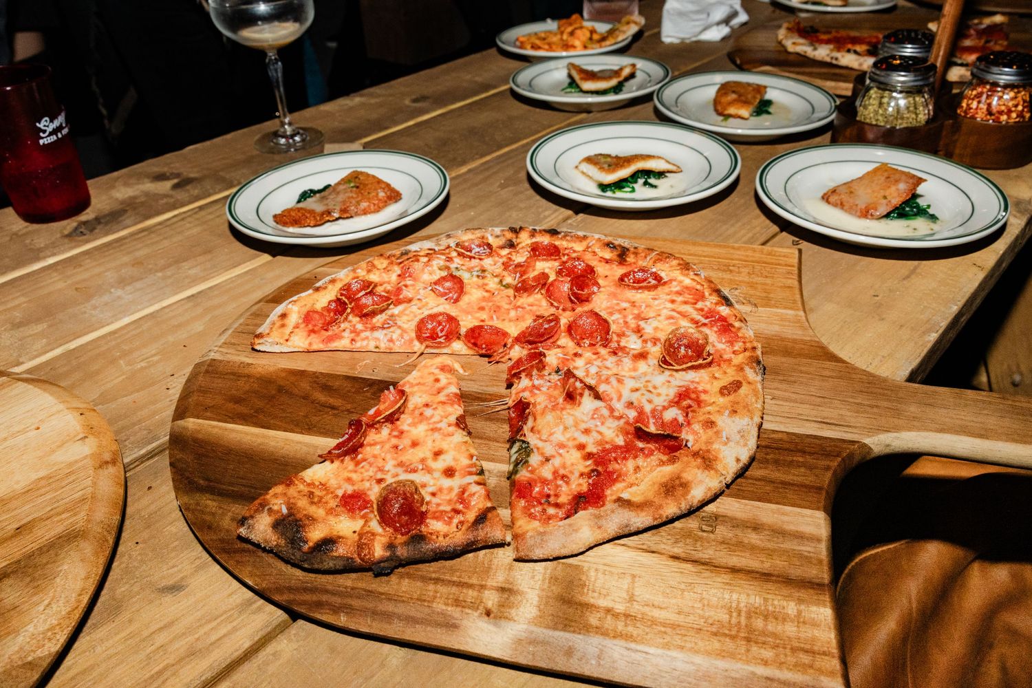 Wood serving boards with fresh pizzas on a rustic wooden table at a casual dining event.