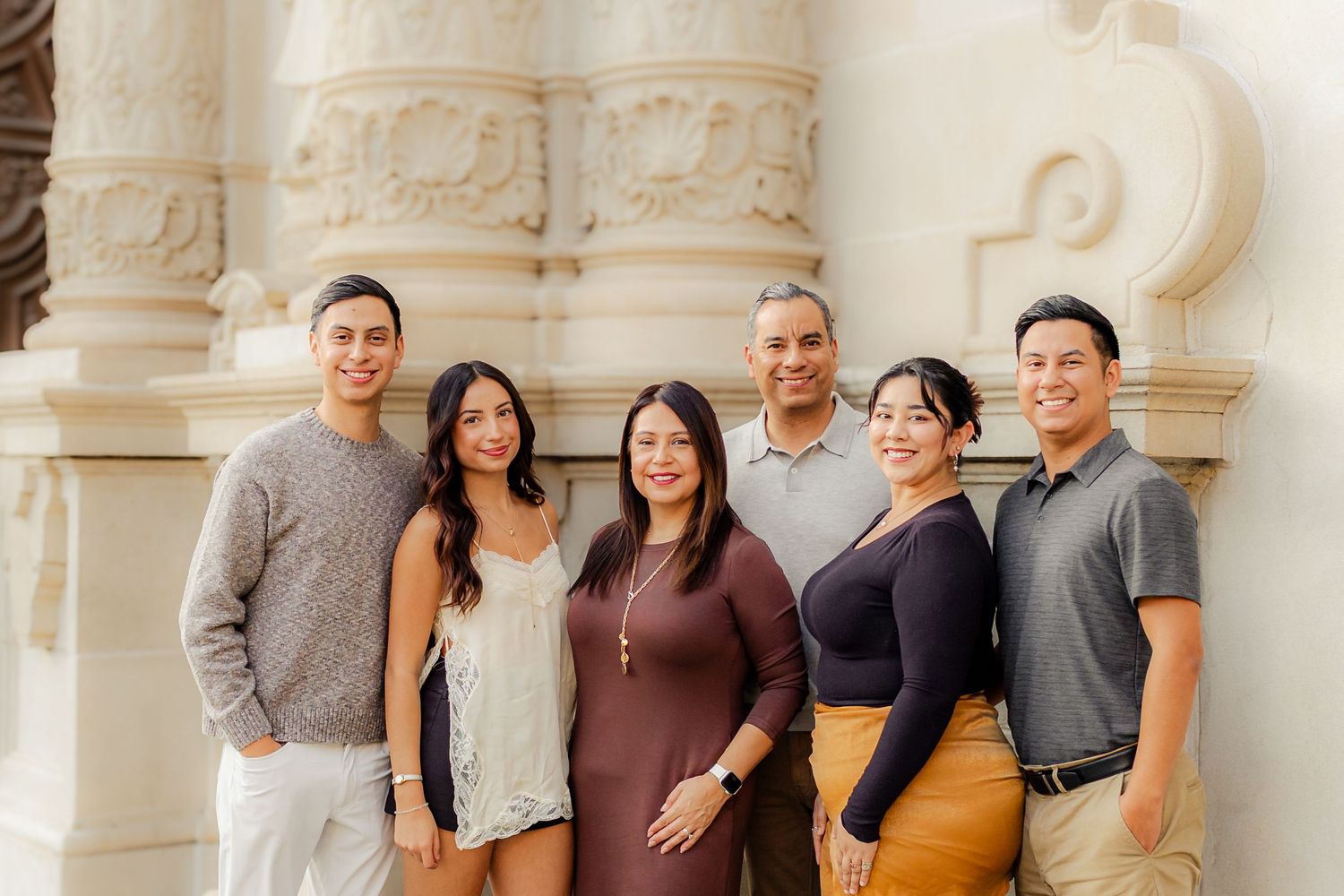 A group of people stand together smiling in front of a white stone building with ornate columns.
