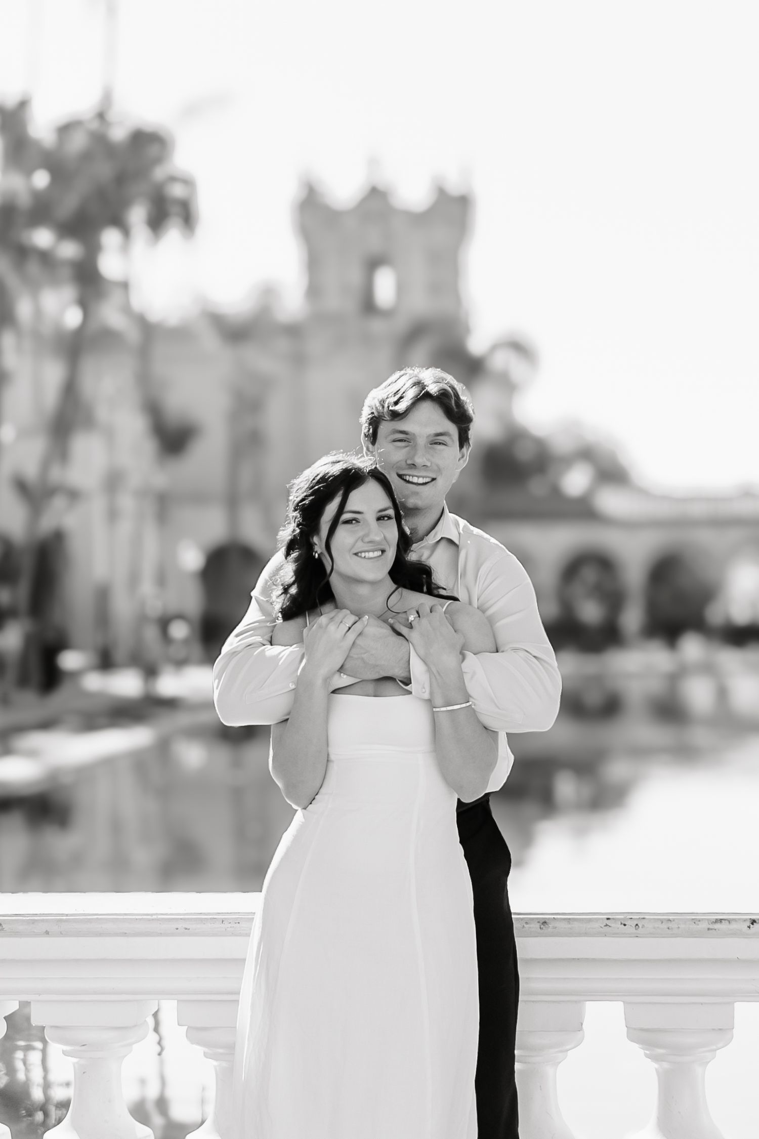 A romantic black and white photo series showing a couple embracing and laughing together on a white balcony.