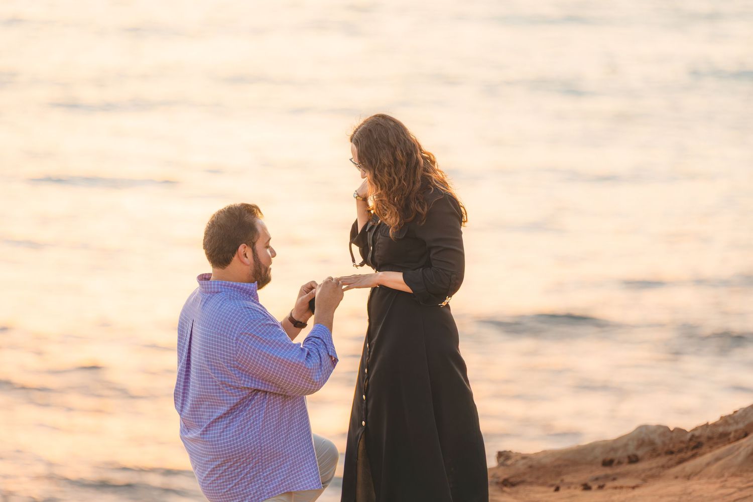 Two people share a romantic moment on coastal cliffs with the sun setting over the Pacific ocean.