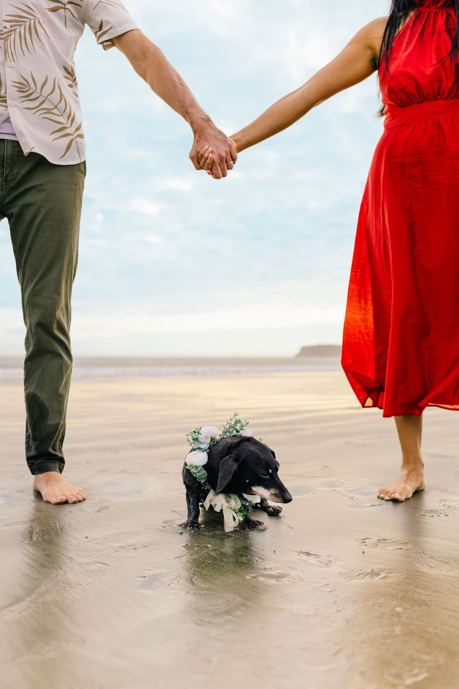 Couple's feet walking together on a wet sandy beach with red dress and casual attire visible.