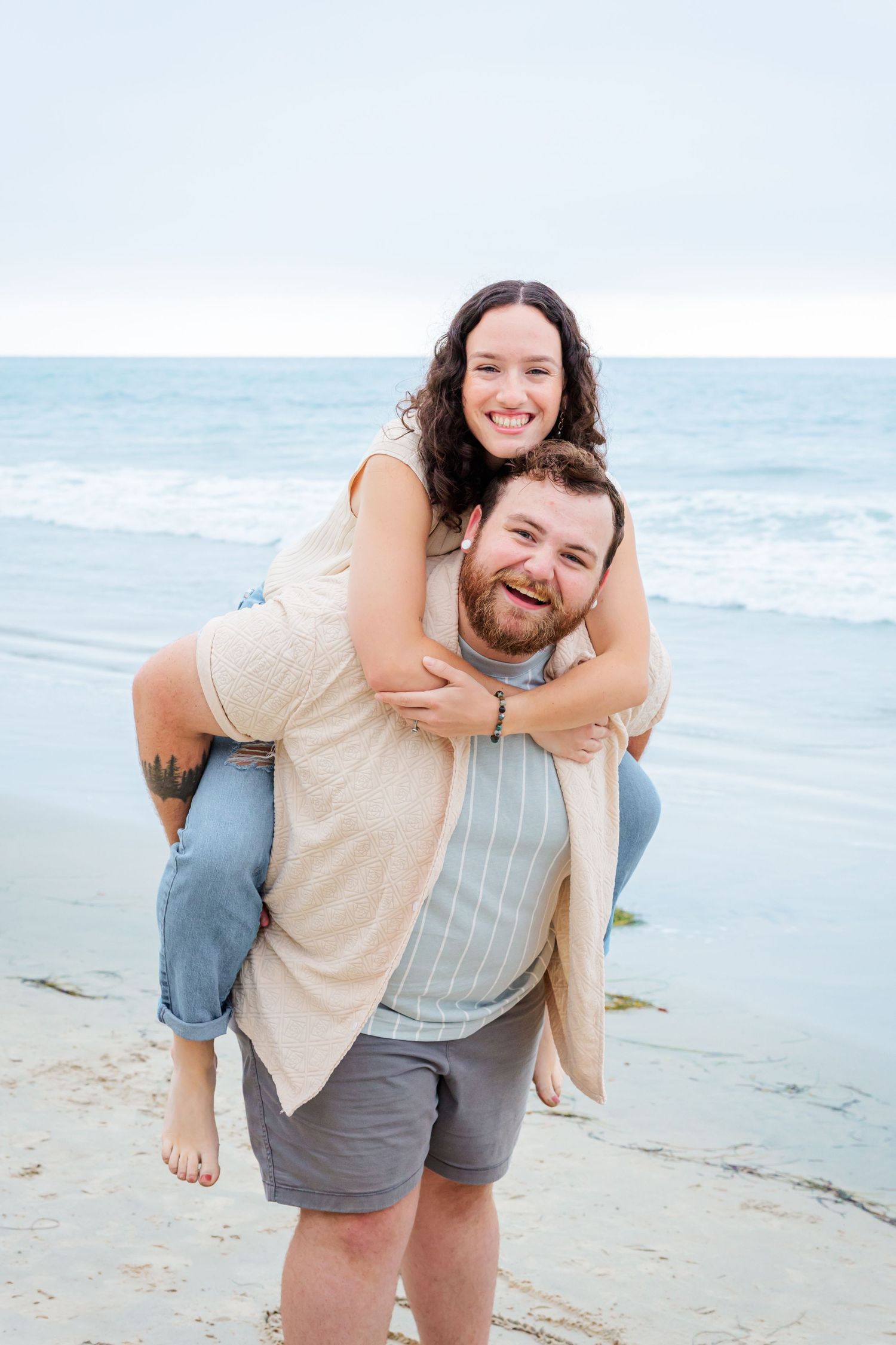 A cheerful piggyback ride moment captured on a sunny beach with waves in the background.
