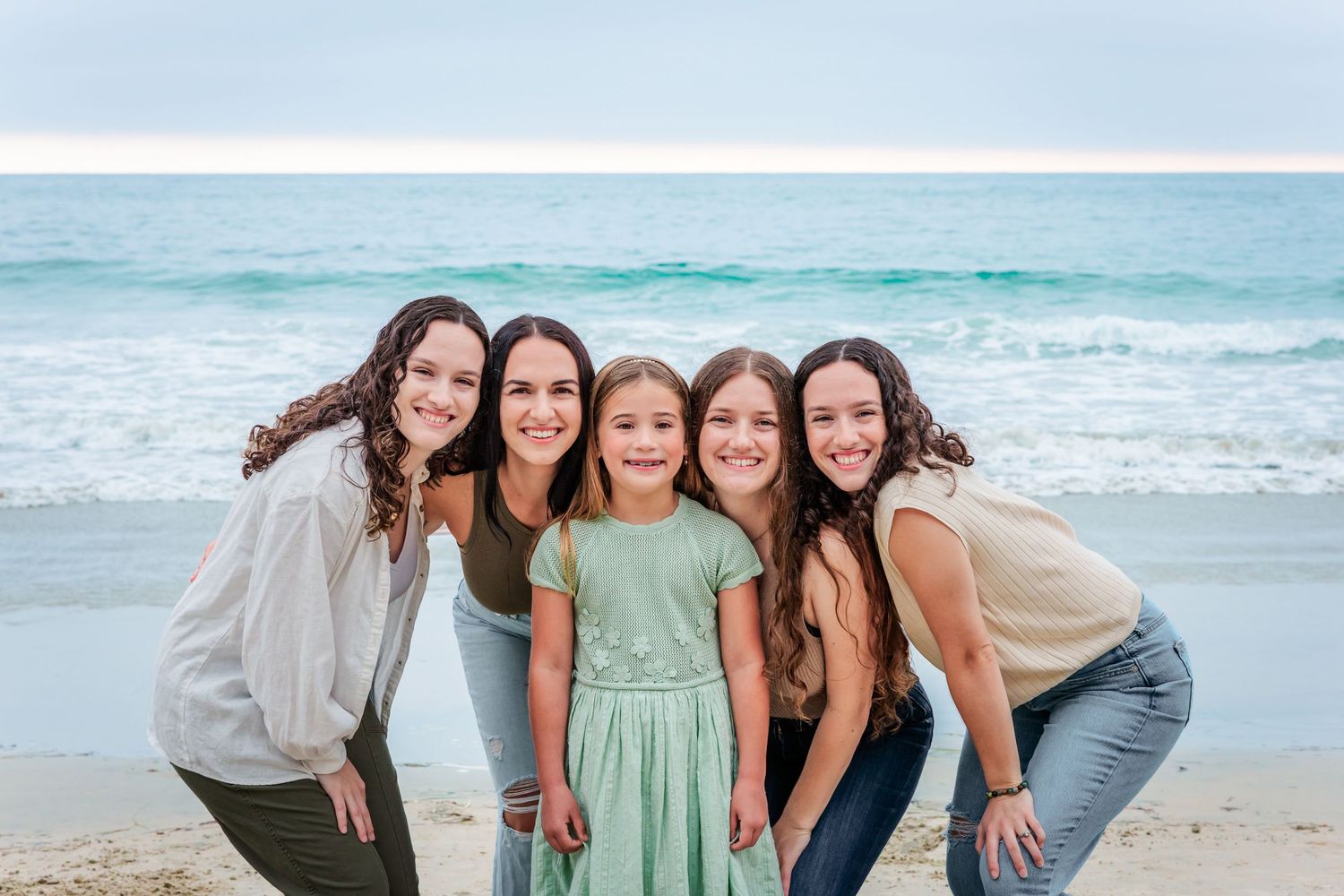 Five people pose together on a beach with crashing waves behind them.