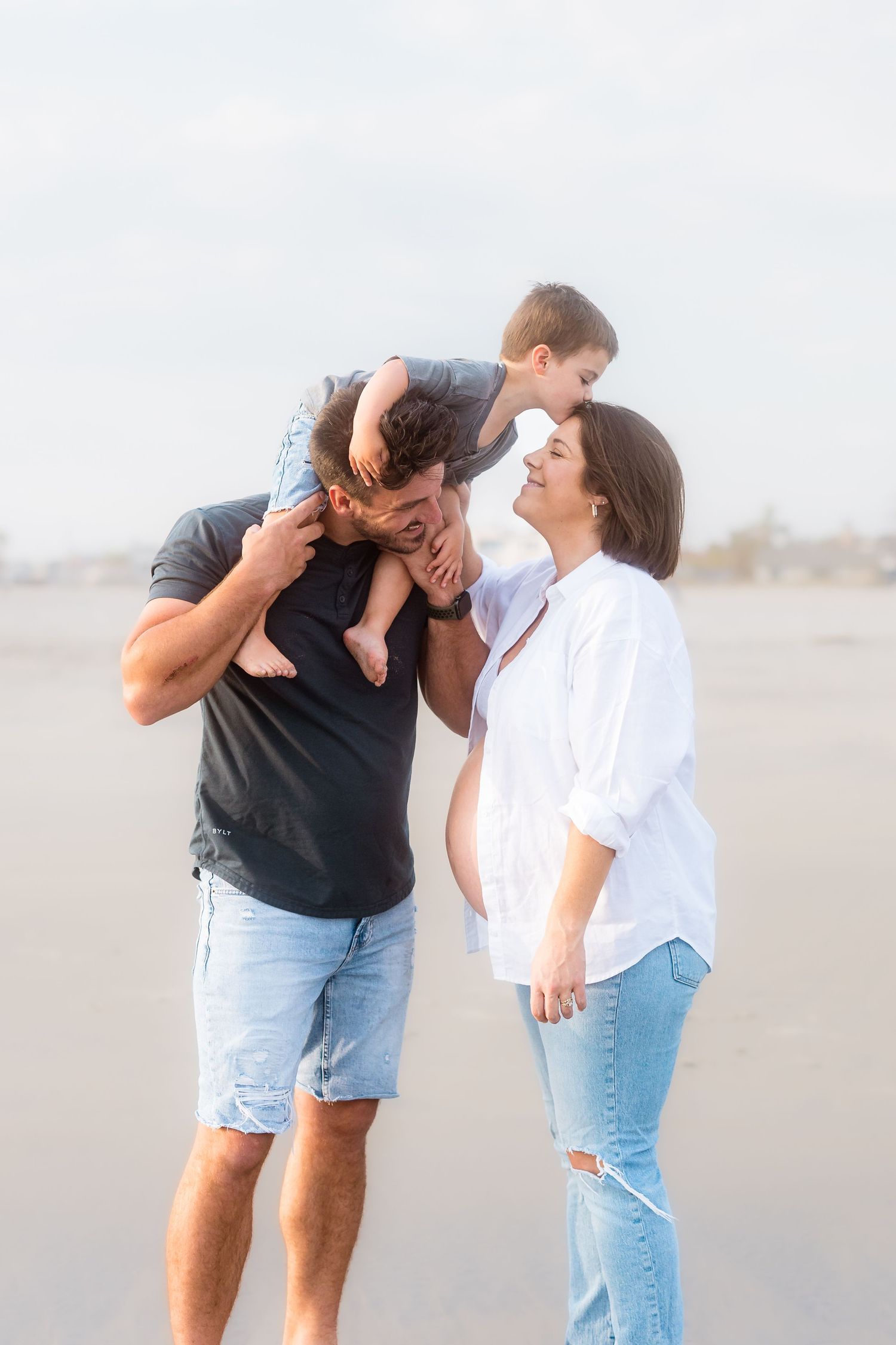 A playful beach photoshoot of a couple sharing intimate moments on a misty shoreline.