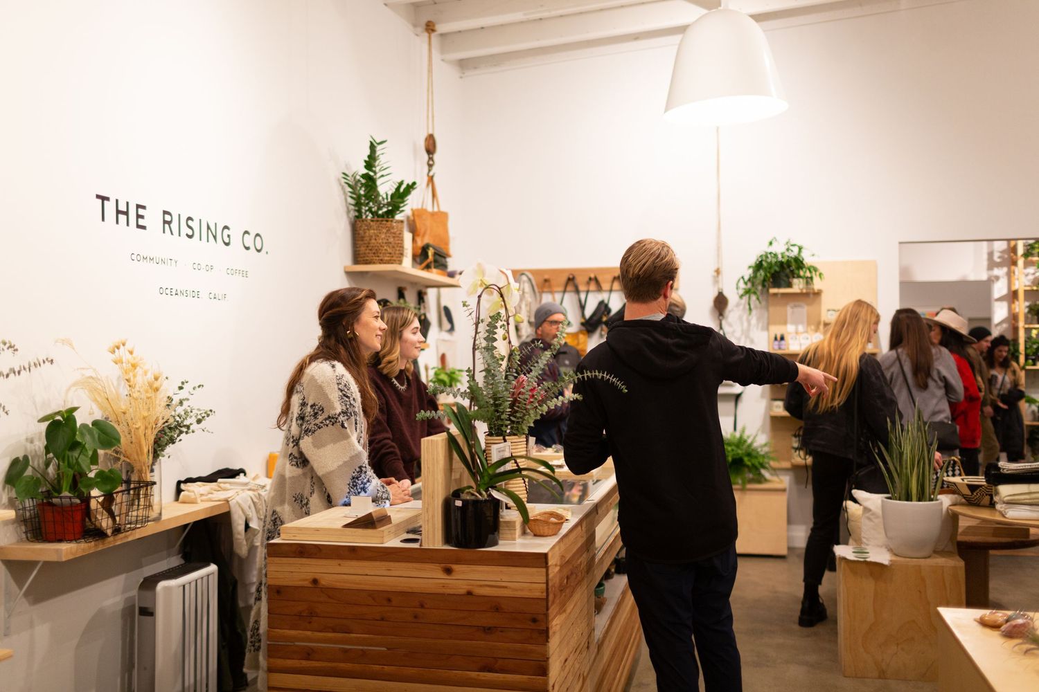 Customers browse products in a modern minimalist retail store with white walls and wood furnishings.