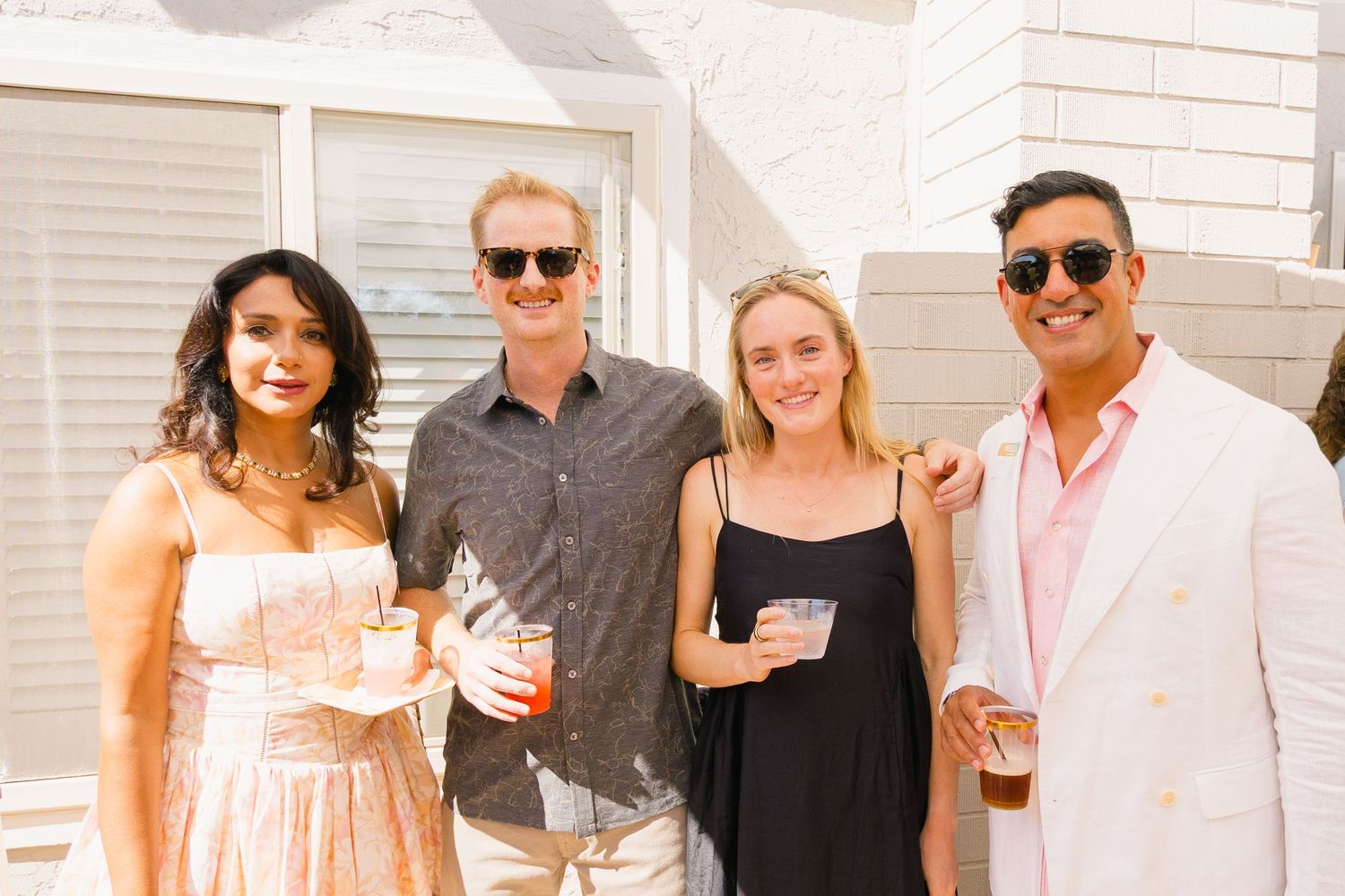 Group of party guests posing together under bright sunlight at an outdoor social event.