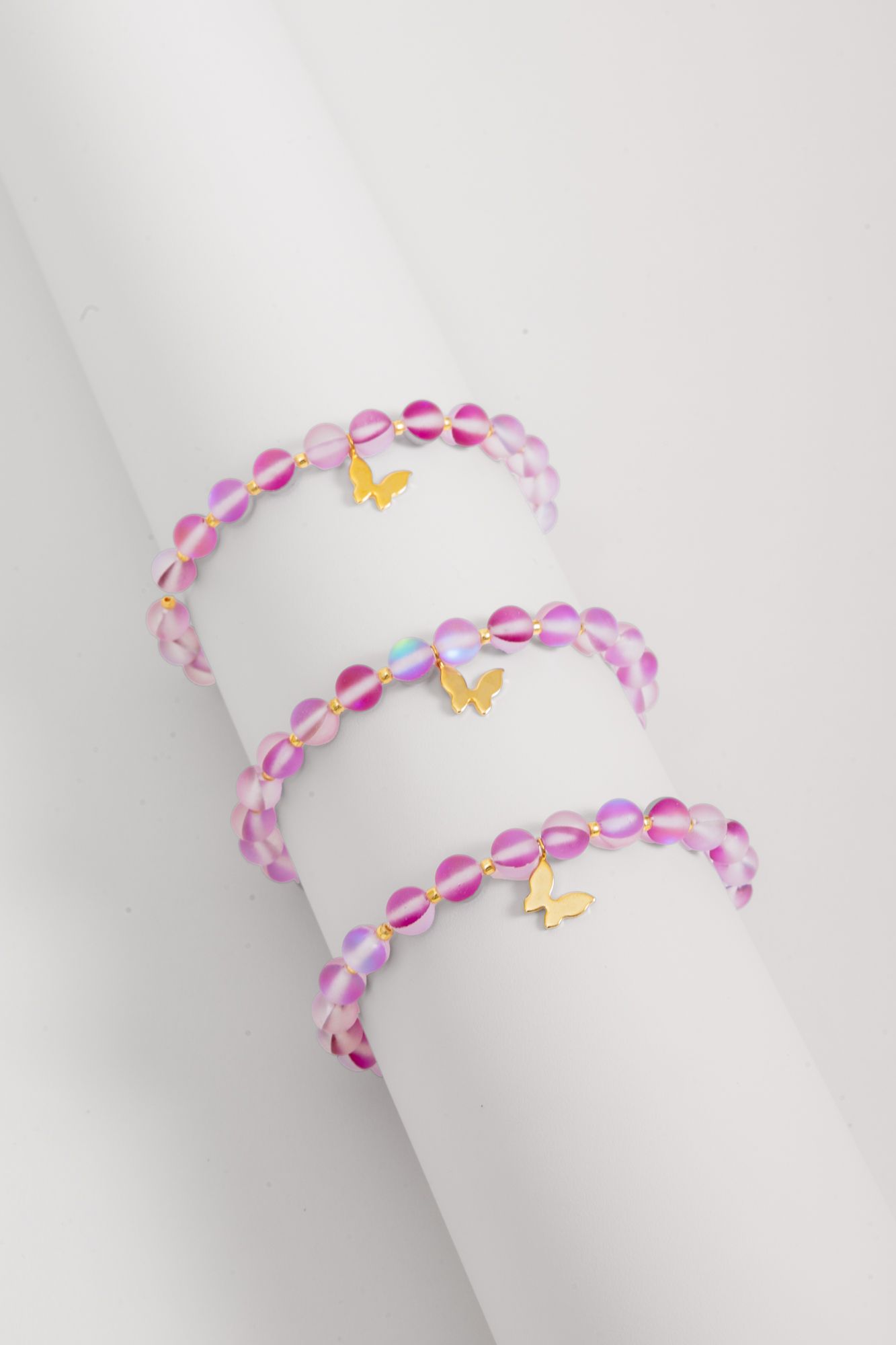 Three pink beaded bracelets with gold butterfly charms on white surface.