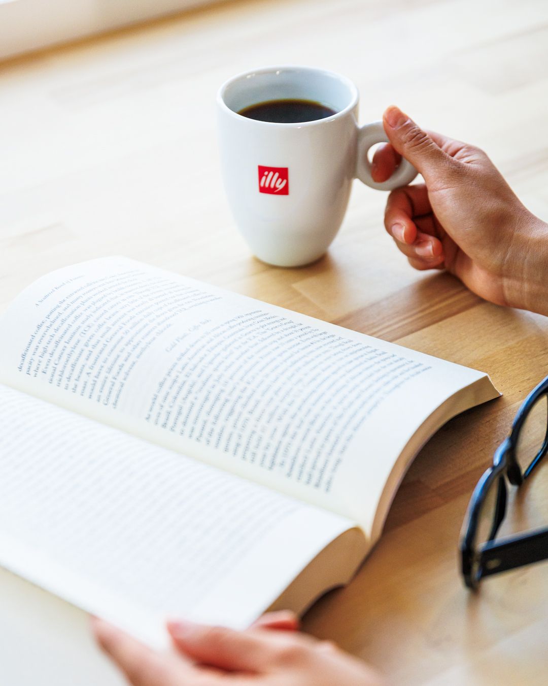 Open book with illy coffee cup on wooden table during relaxing reading time.