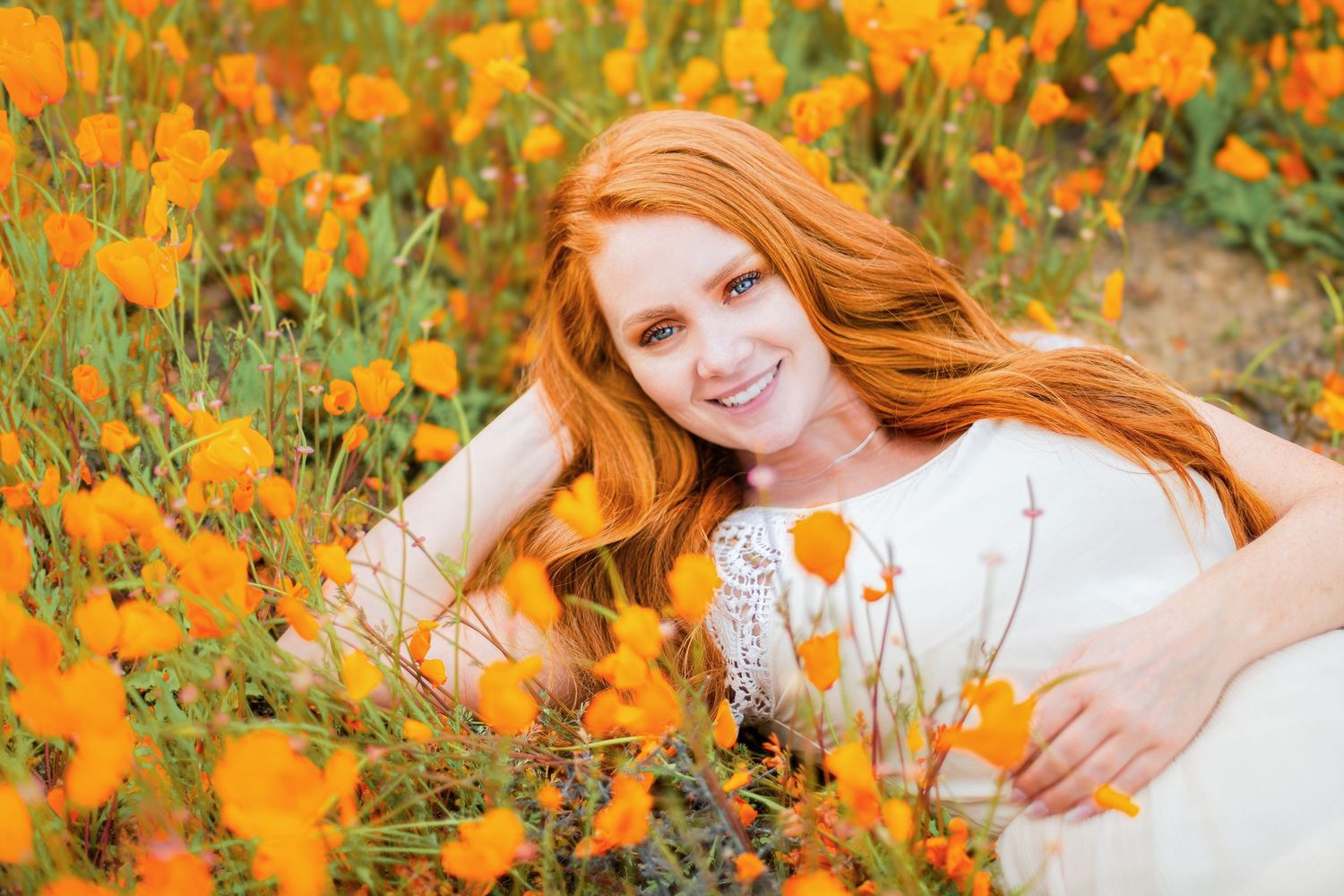 Woman lying in field of bright orange California poppies wearing white lace dress.