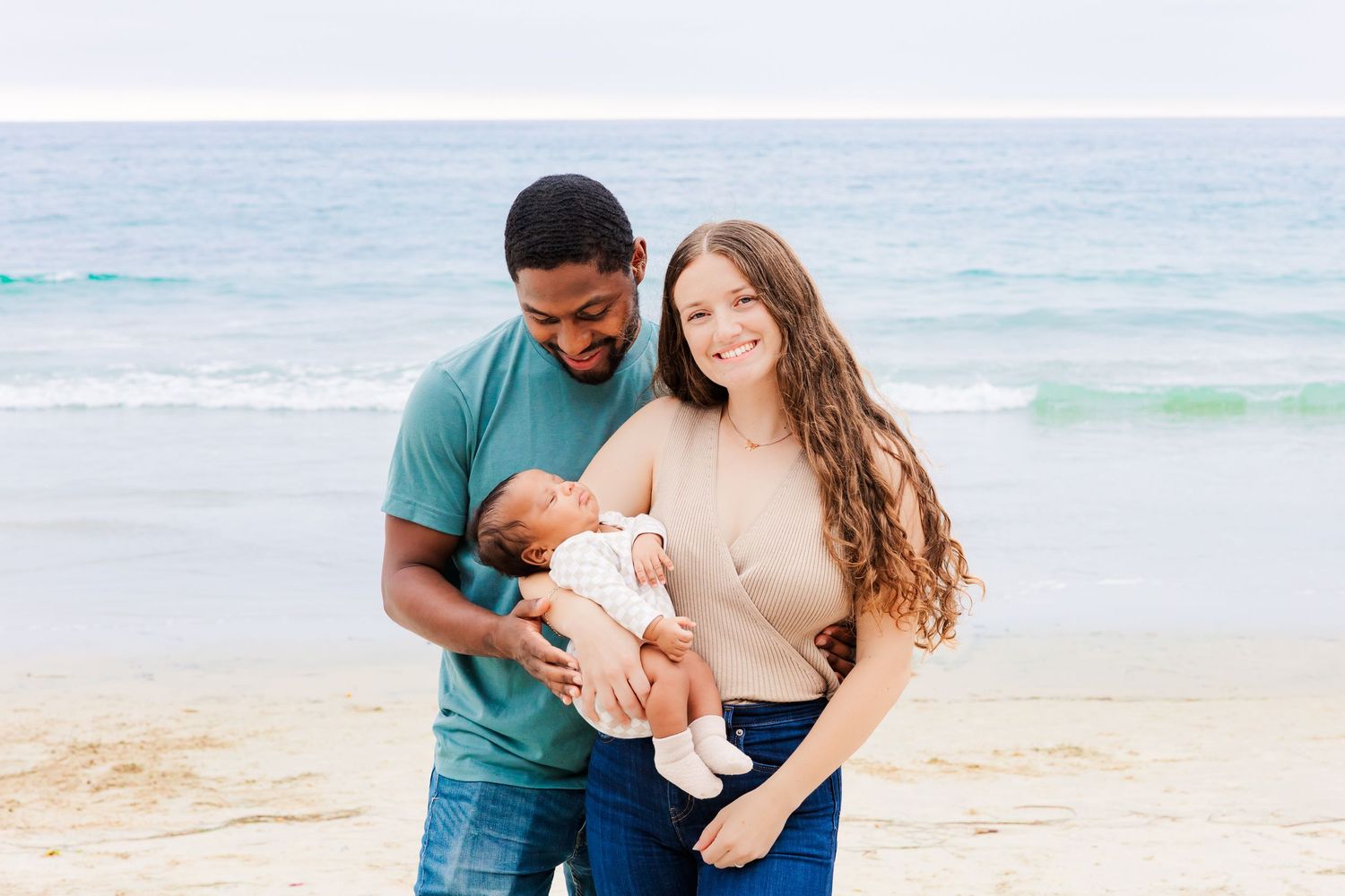 Parents cradling their newborn baby on a peaceful beach setting.