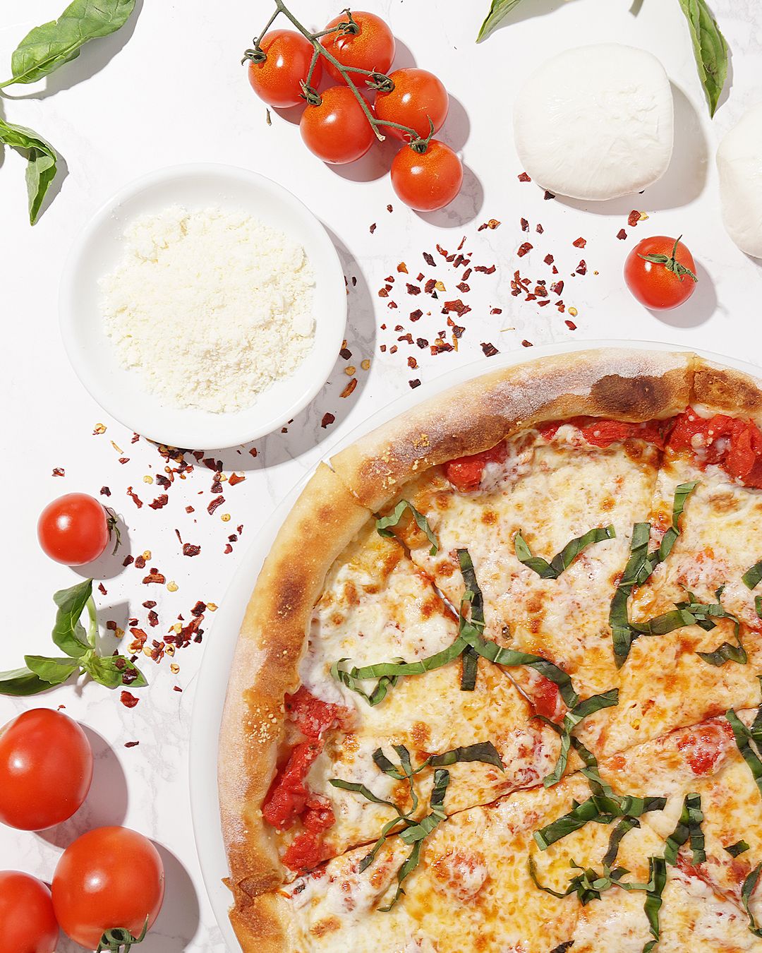 Fresh pizza with cherry tomatoes, mozzarella, and herbs arranged on a white surface.