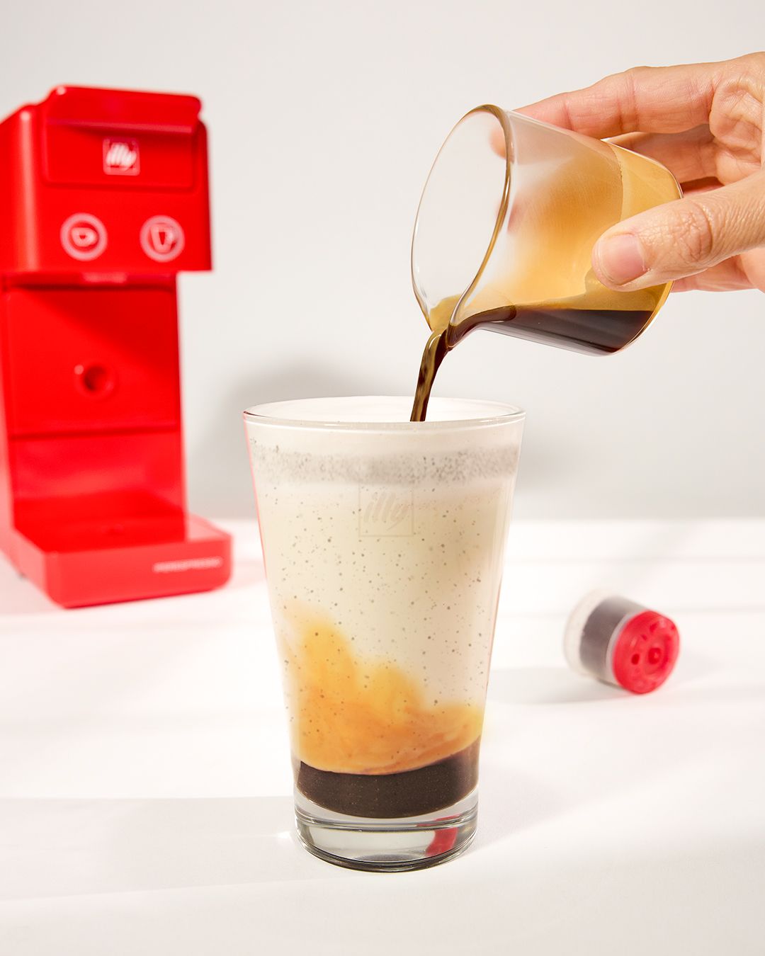 Coffee being poured into glass creating a layered effect against white background.