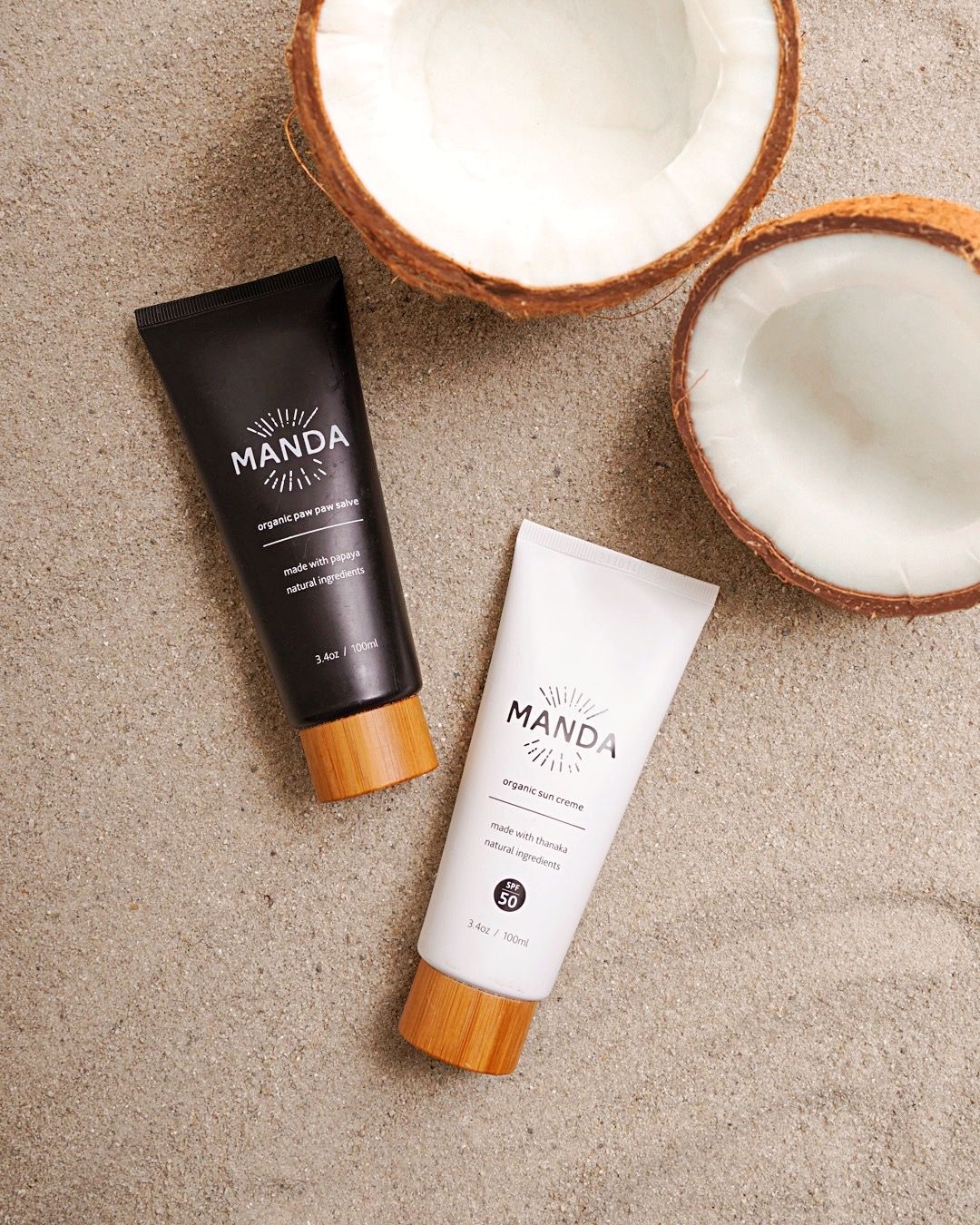 Manda beauty products displayed with fresh coconut halves on beige background.
