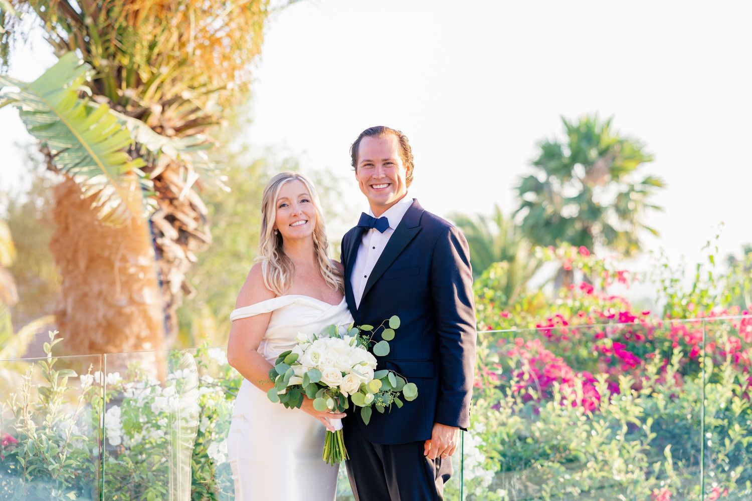 Elegant wedding photos captured on a terrace with colorful flowers and palm trees in the background.