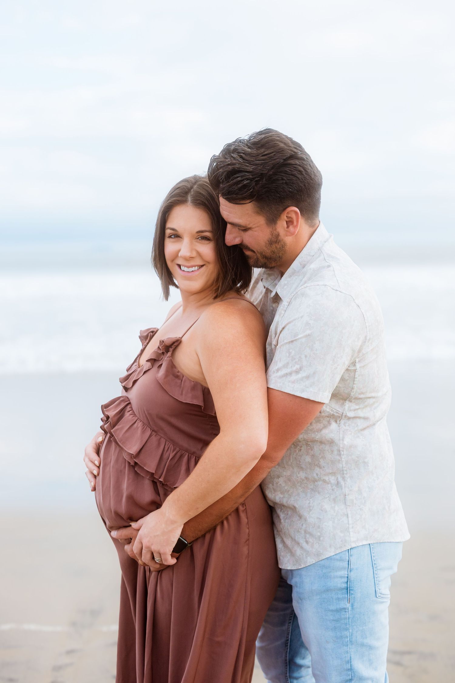 Intimate beach maternity photo with couple embracing in casual attire.