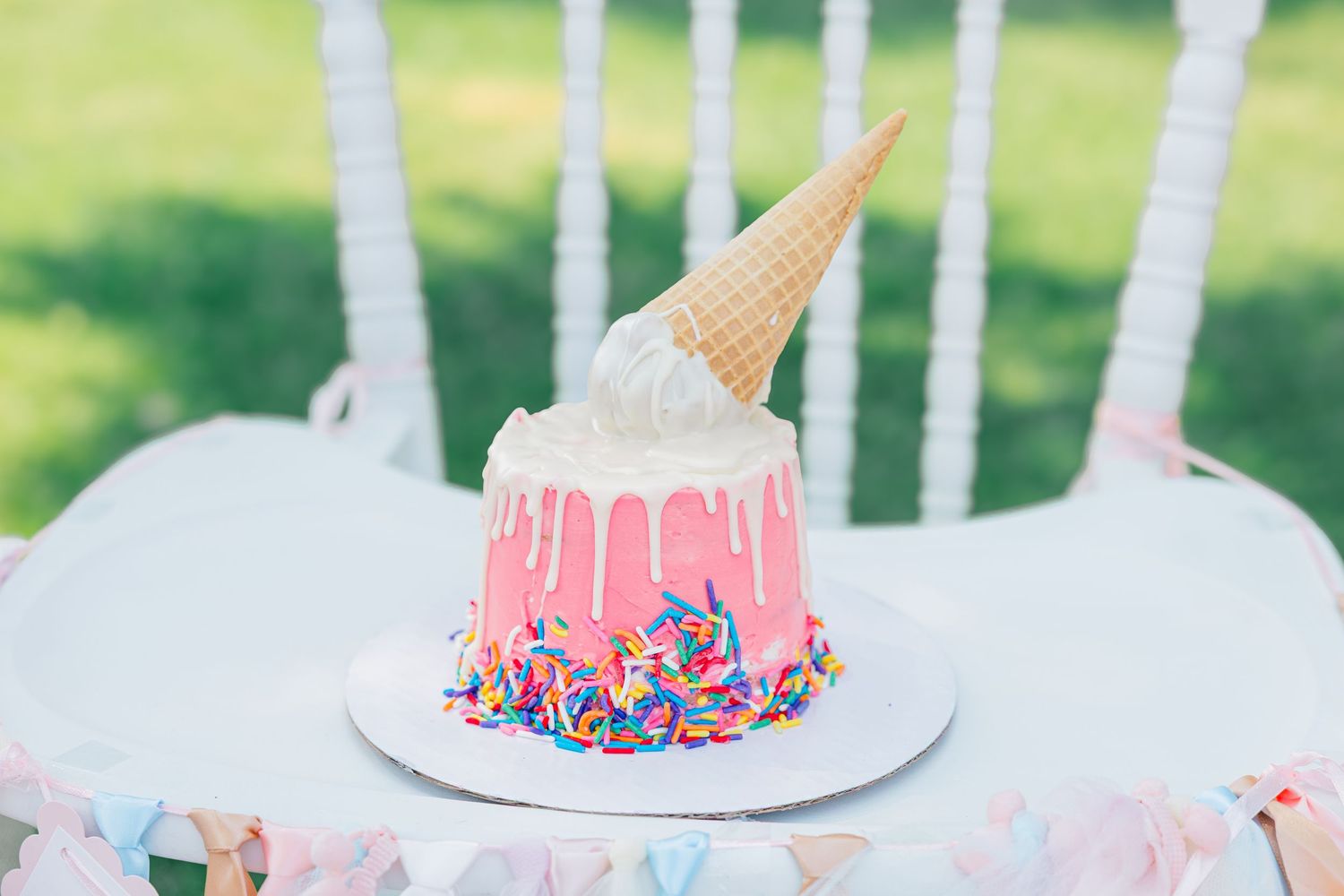 White outdoor party table decorated with pink and blue cupcakes and desserts for a festive celebration.