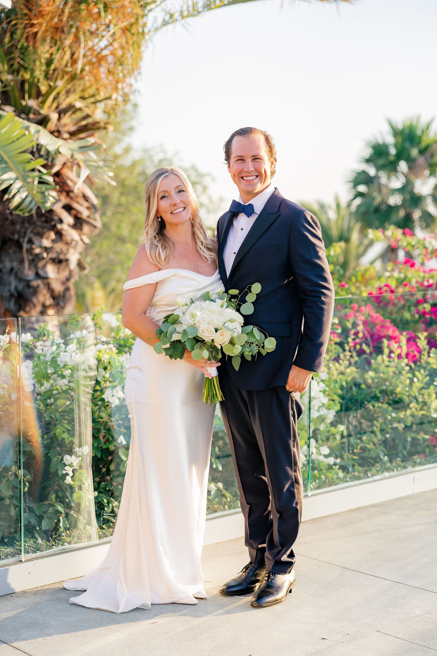 A wedding couple poses in front of lush tropical gardens on a sunny terrace.