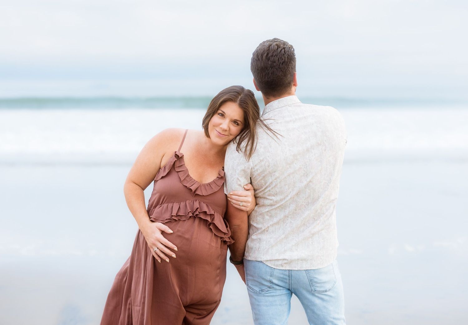 Couple shares intimate moment on beach while expecting new addition to family.