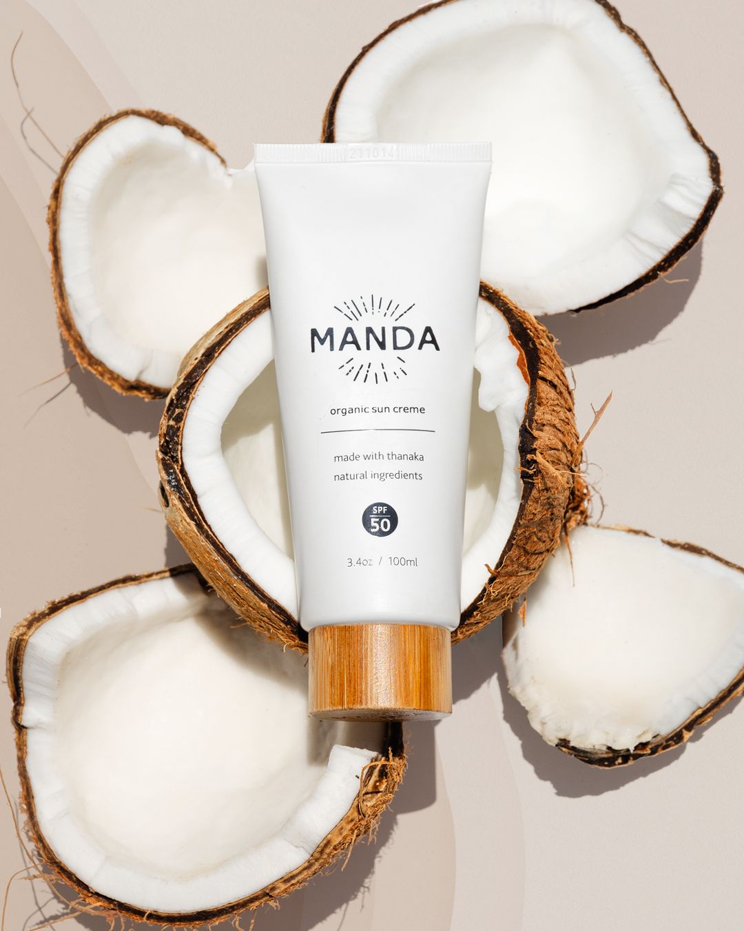 White Manda skincare product tube displayed with fresh coconut halves on beige background.