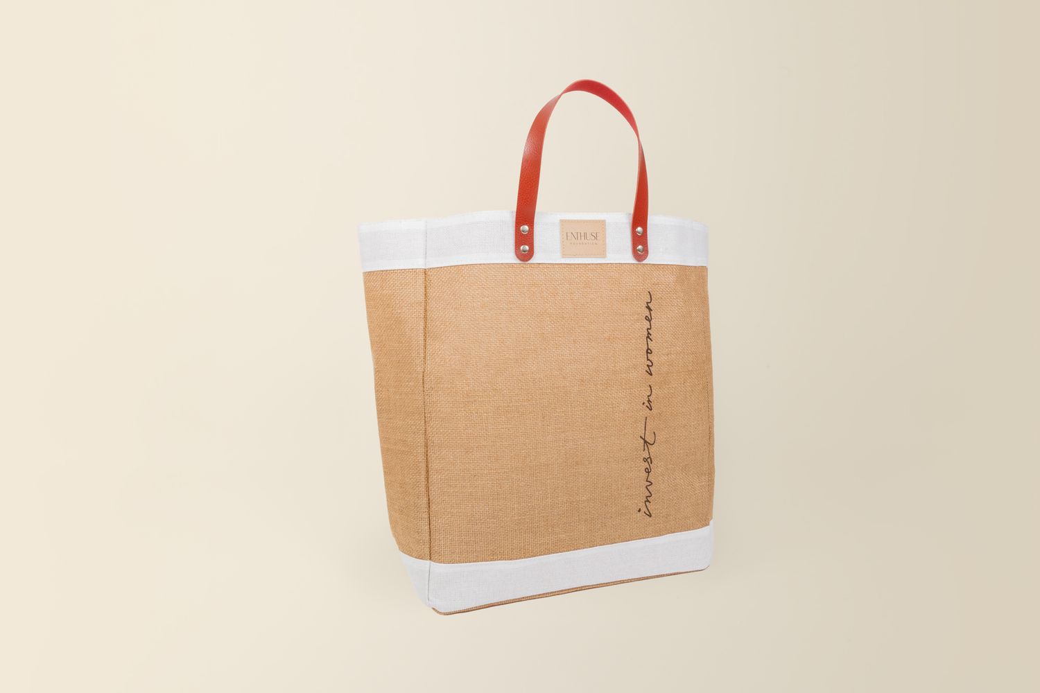 Minimalist tote bag made from tan canvas with white trim and red handles against beige background.