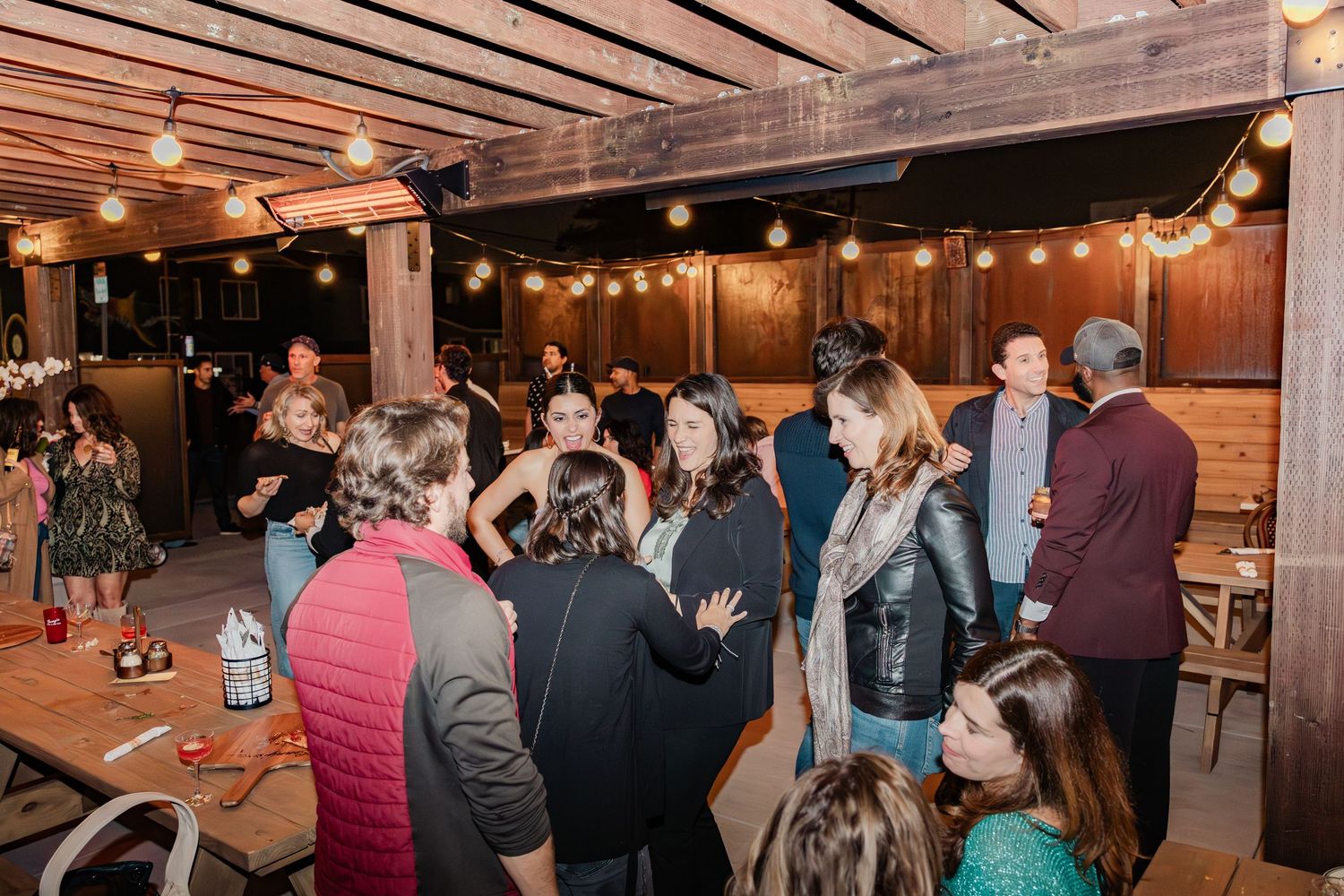 Crowded indoor venue with wooden ceiling beams and string lights creating a warm atmosphere.