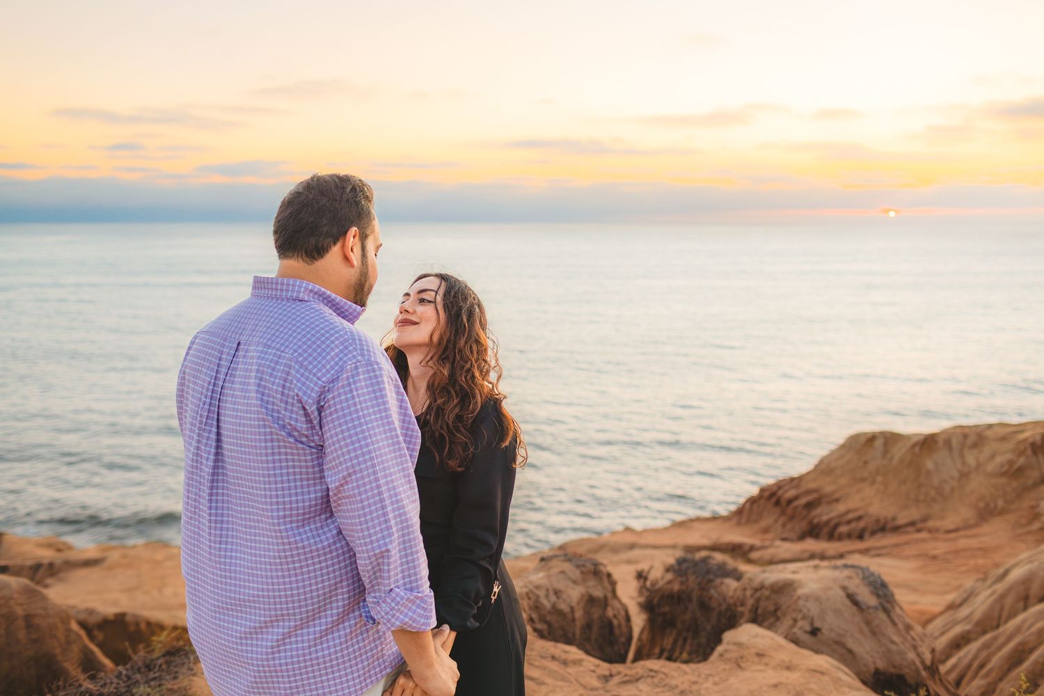 A couple shares a romantic moment at sunset on a coastal cliff overlooking the ocean.