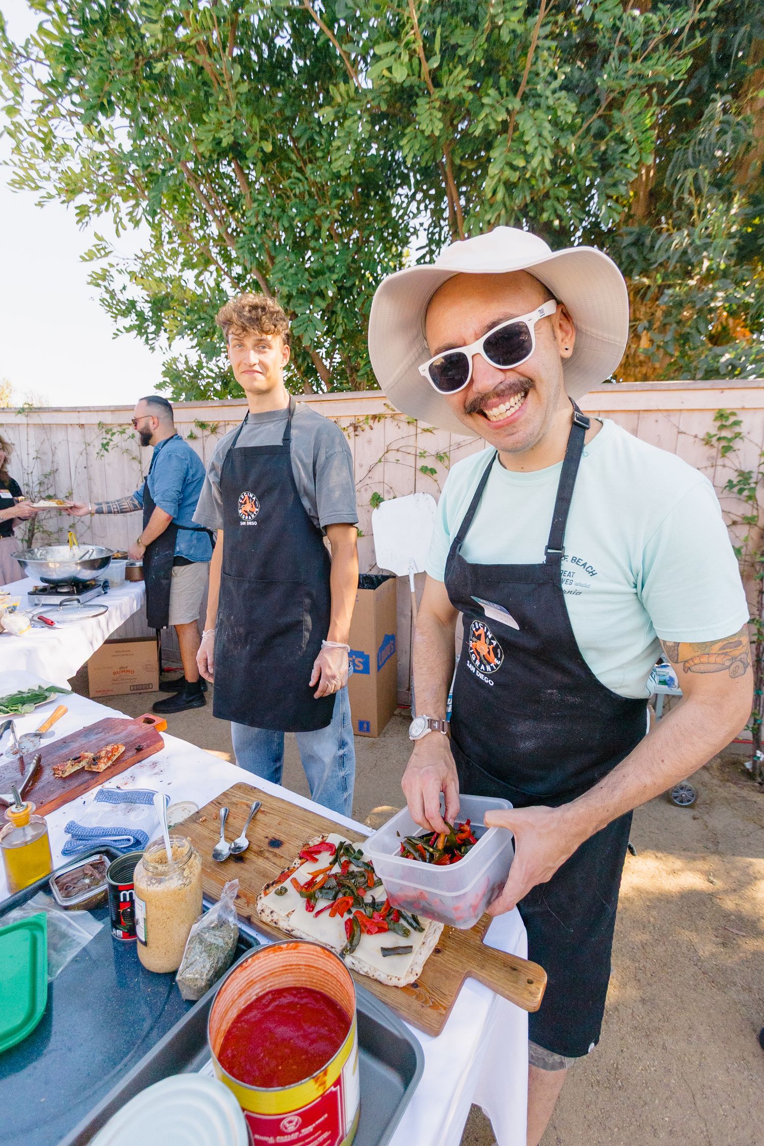 People in aprons preparing food and drinks at an outdoor serving station.