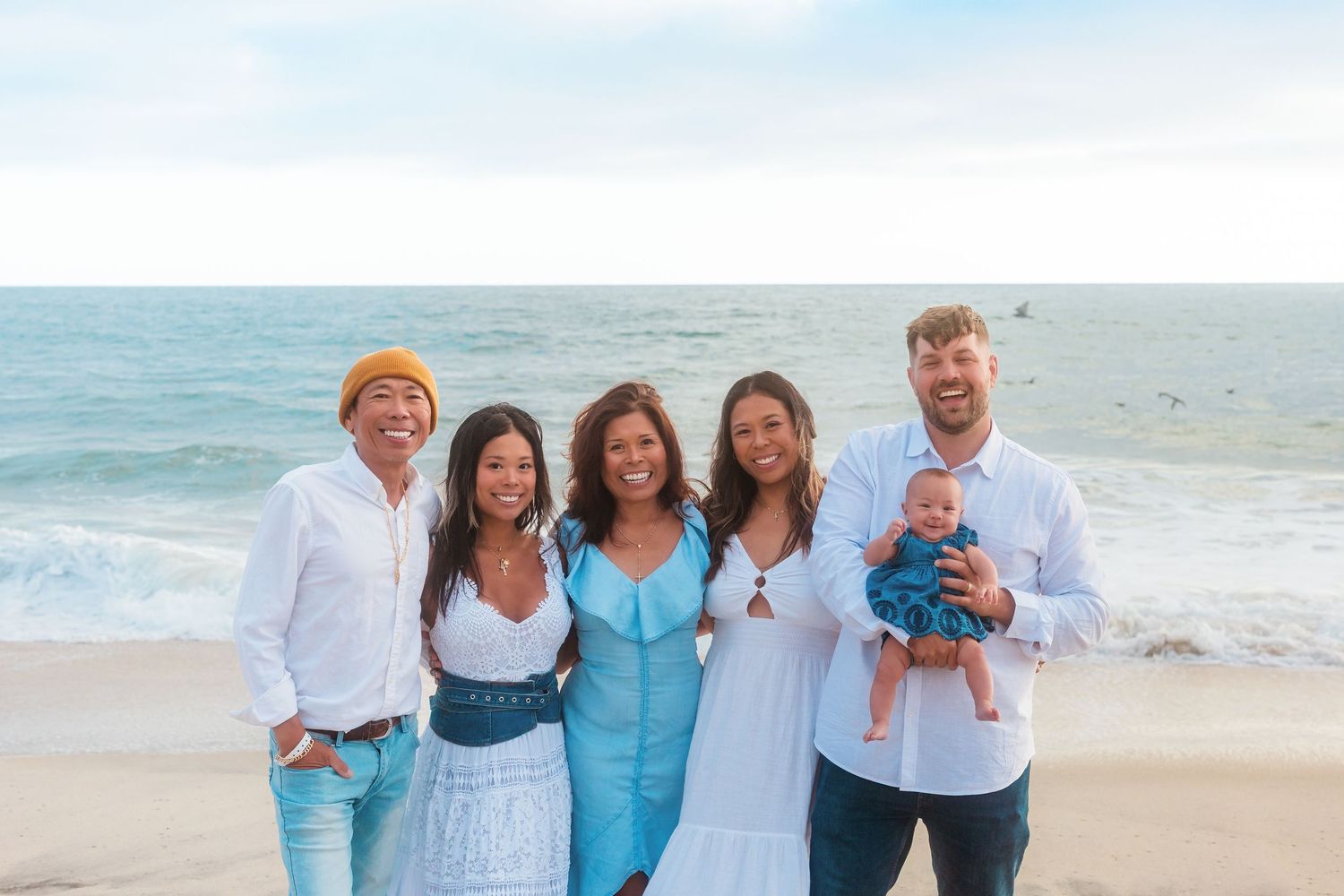 Group poses together on sunny beach in casual white and blue summer outfits.