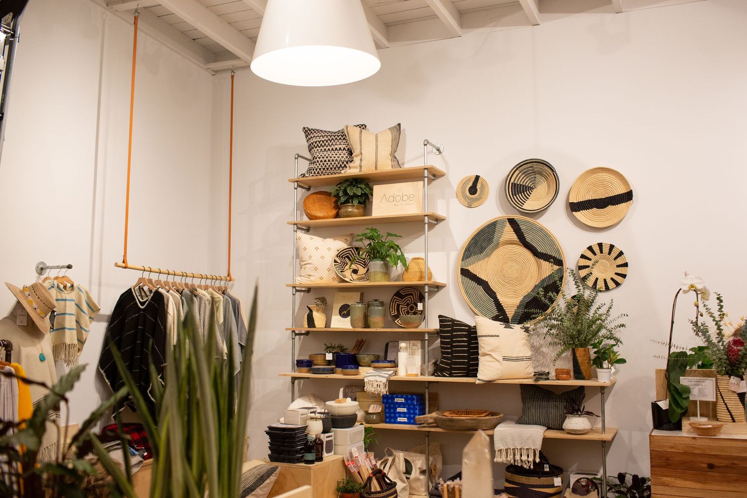 A bright and airy retail store interior displays home decor items, furniture, and plants on wooden shelves and tables.