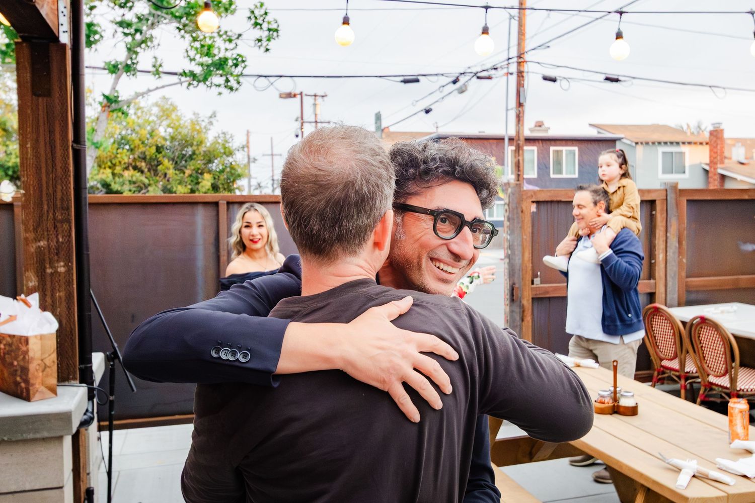 Two people sharing a warm embrace at an outdoor restaurant patio.