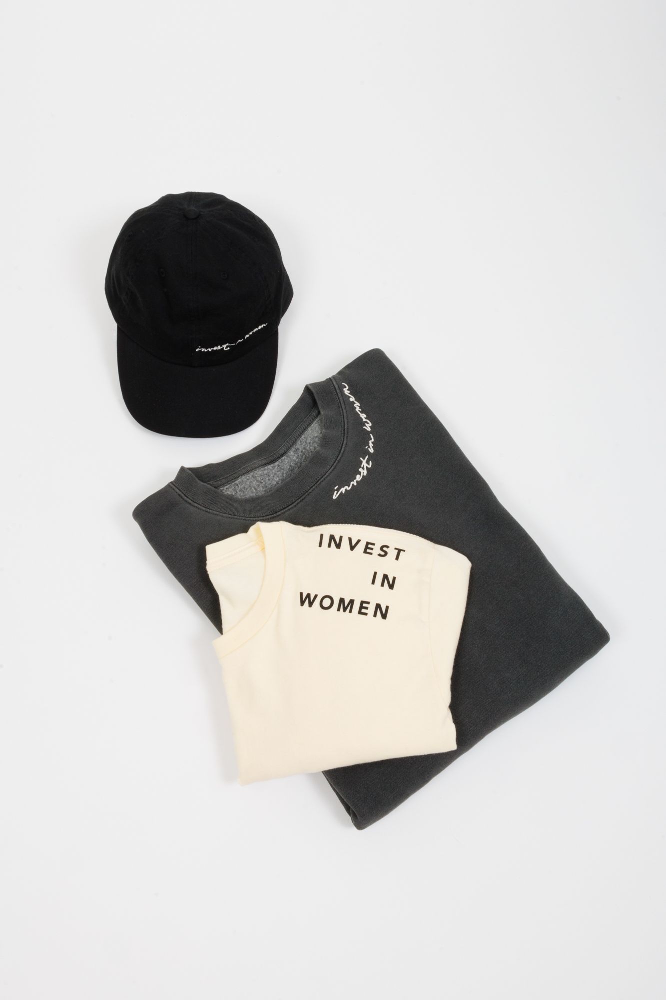 Flat lay of black cap, black sweatshirt, and white t-shirt with text design.