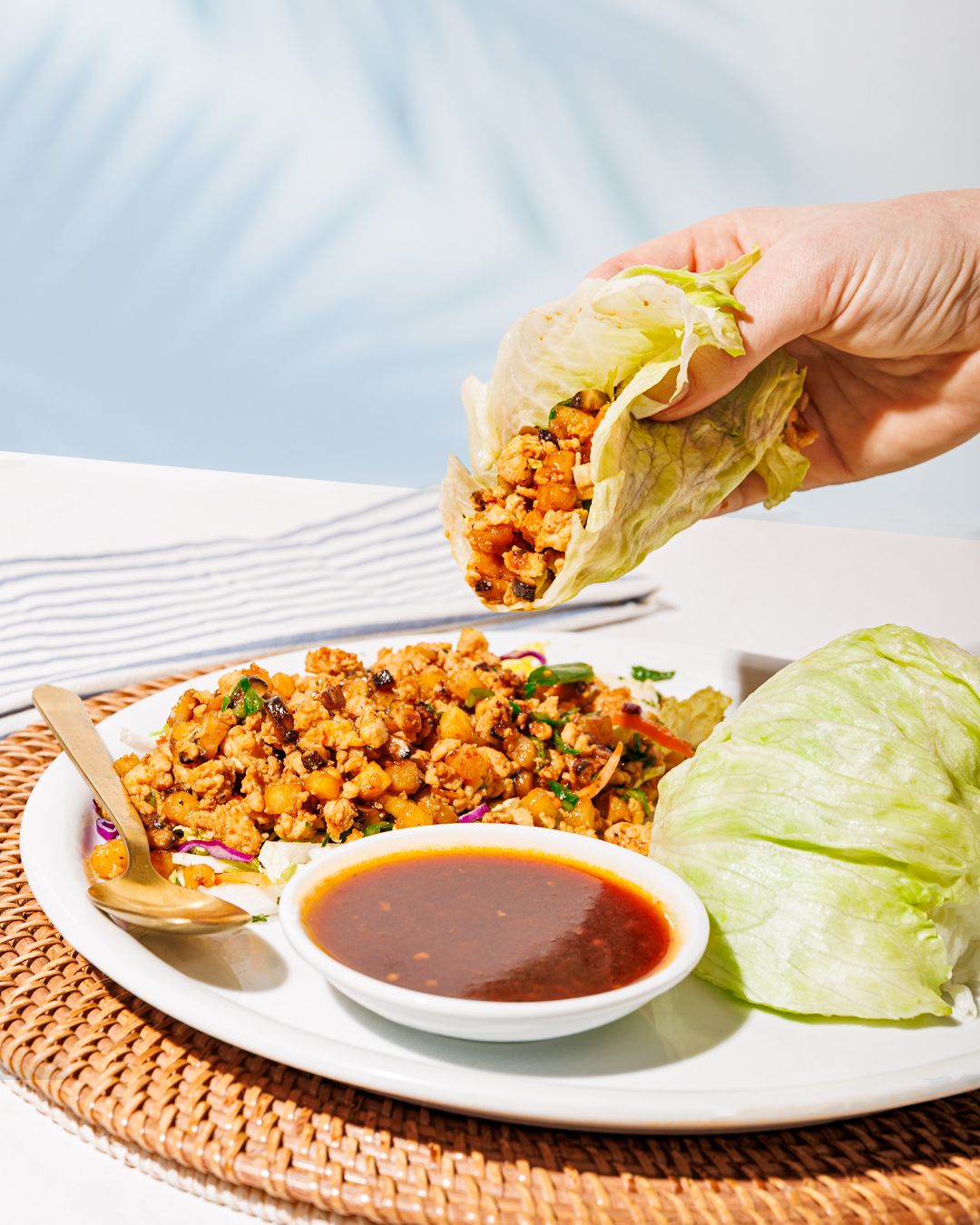Lettuce wraps with spicy ground meat filling and dipping sauce served on woven placemats.