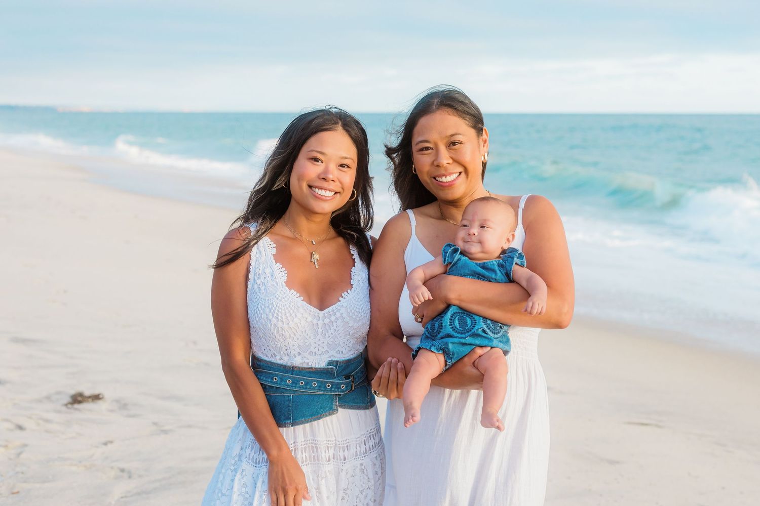 Three people share a joyful moment on the beach with the ocean waves behind them.