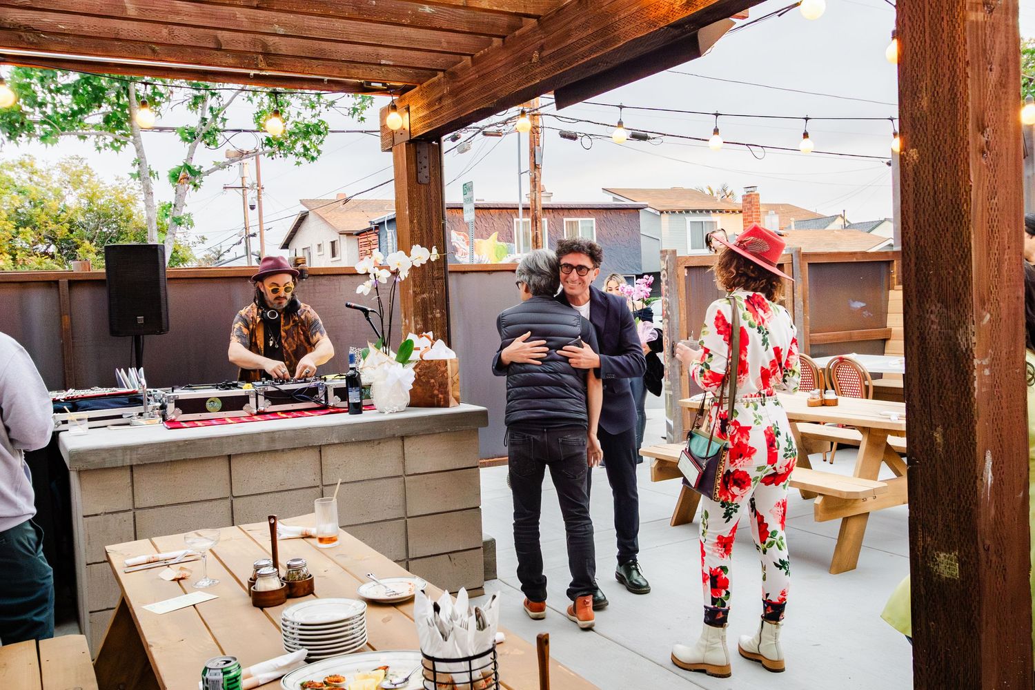 People mingling and celebrating at a rustic outdoor party venue with string lights and wooden beams.