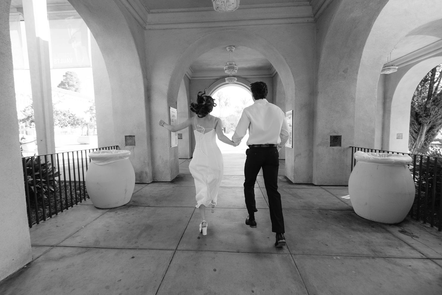 People walk through a white arched colonnade hallway with dramatic shadows cast across the floor.