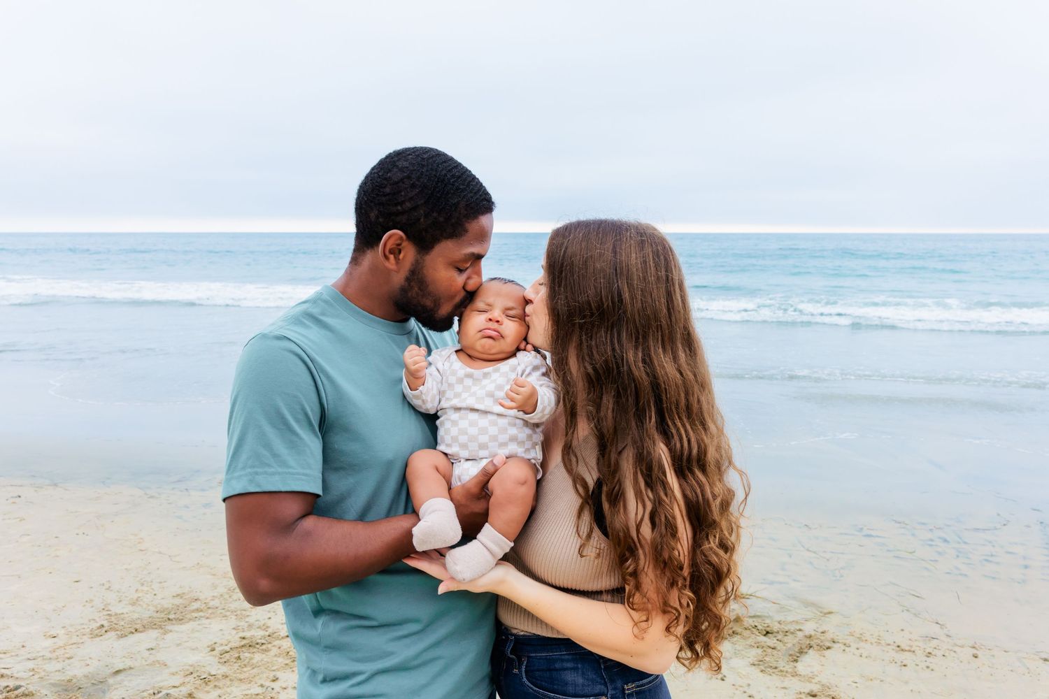 Parents sharing a tender moment with their infant on a scenic beach.