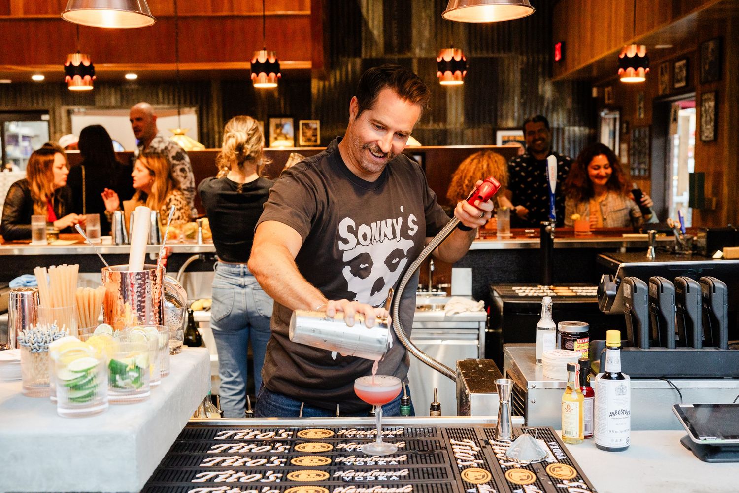 A bartender prepares drinks at a busy restaurant bar under warm lighting.