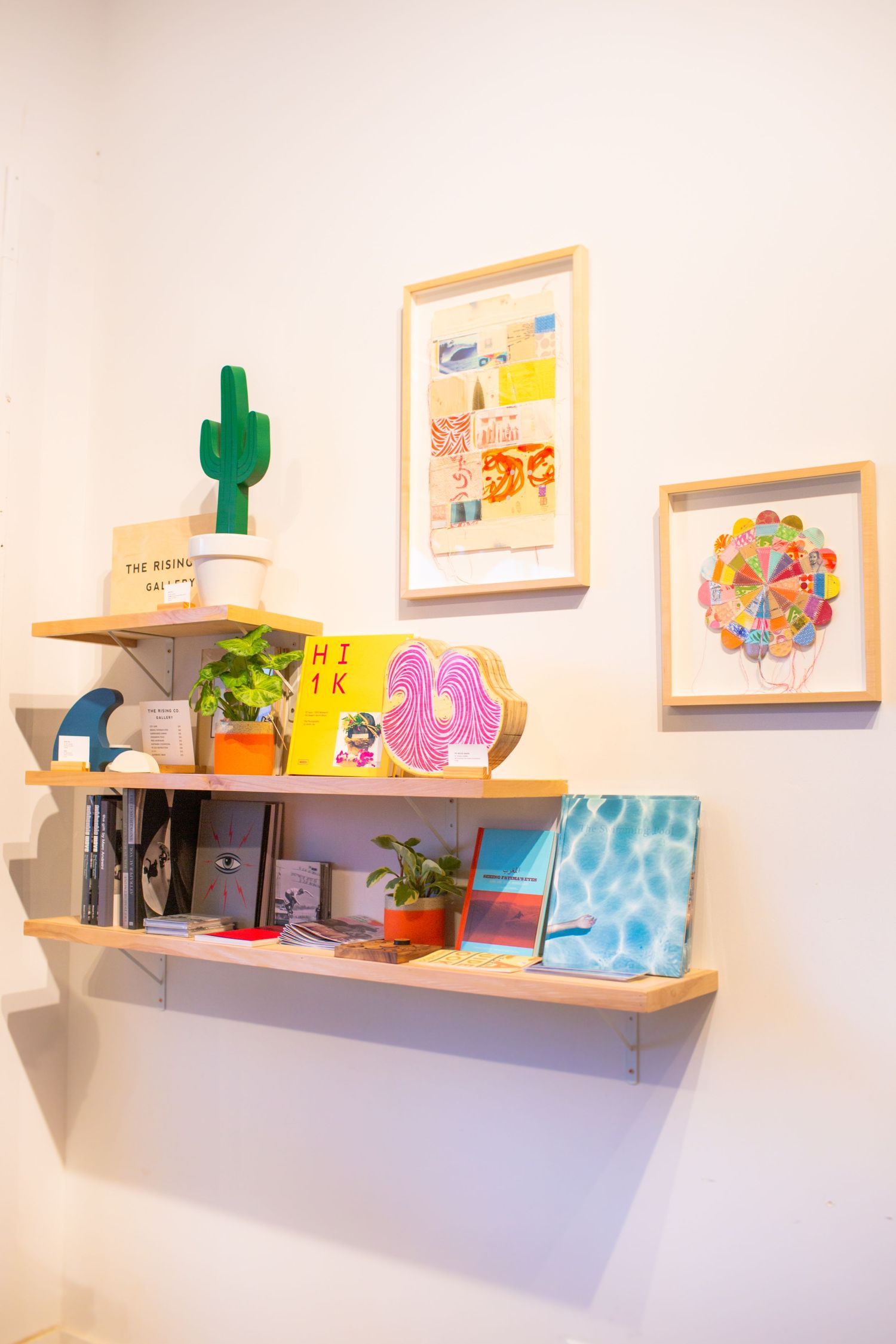 Floating wall shelves display colorful art prints, small potted plants, and decorative objects against a white wall.
