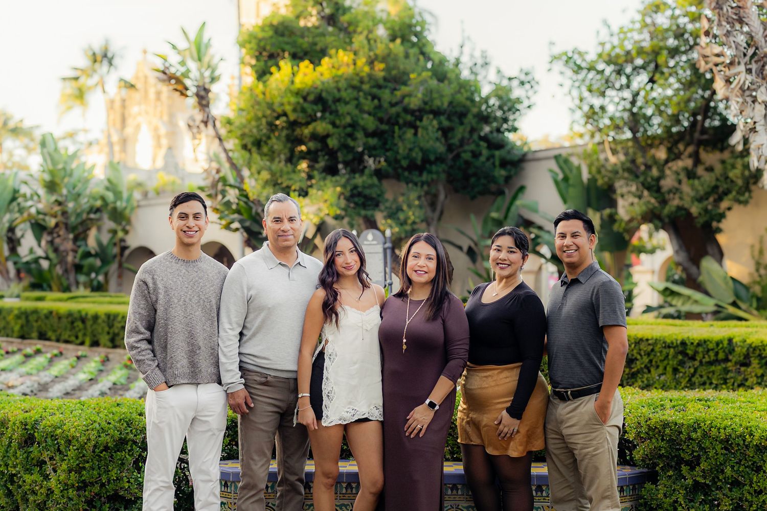 Extended family gathering outdoors in a lush garden setting with palm trees and greenery.