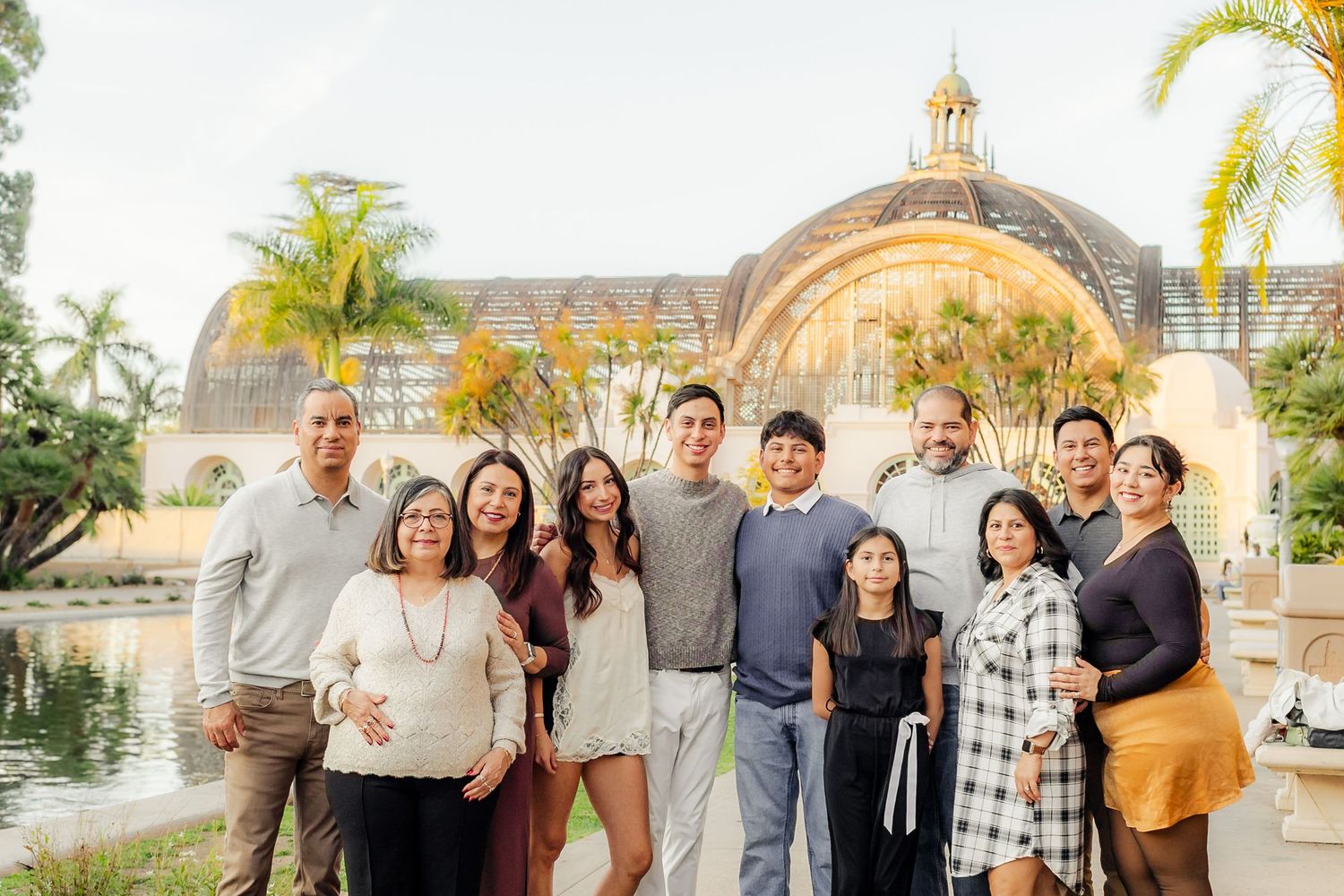A group of people pose together outdoors near palm trees and a church building at sunset.