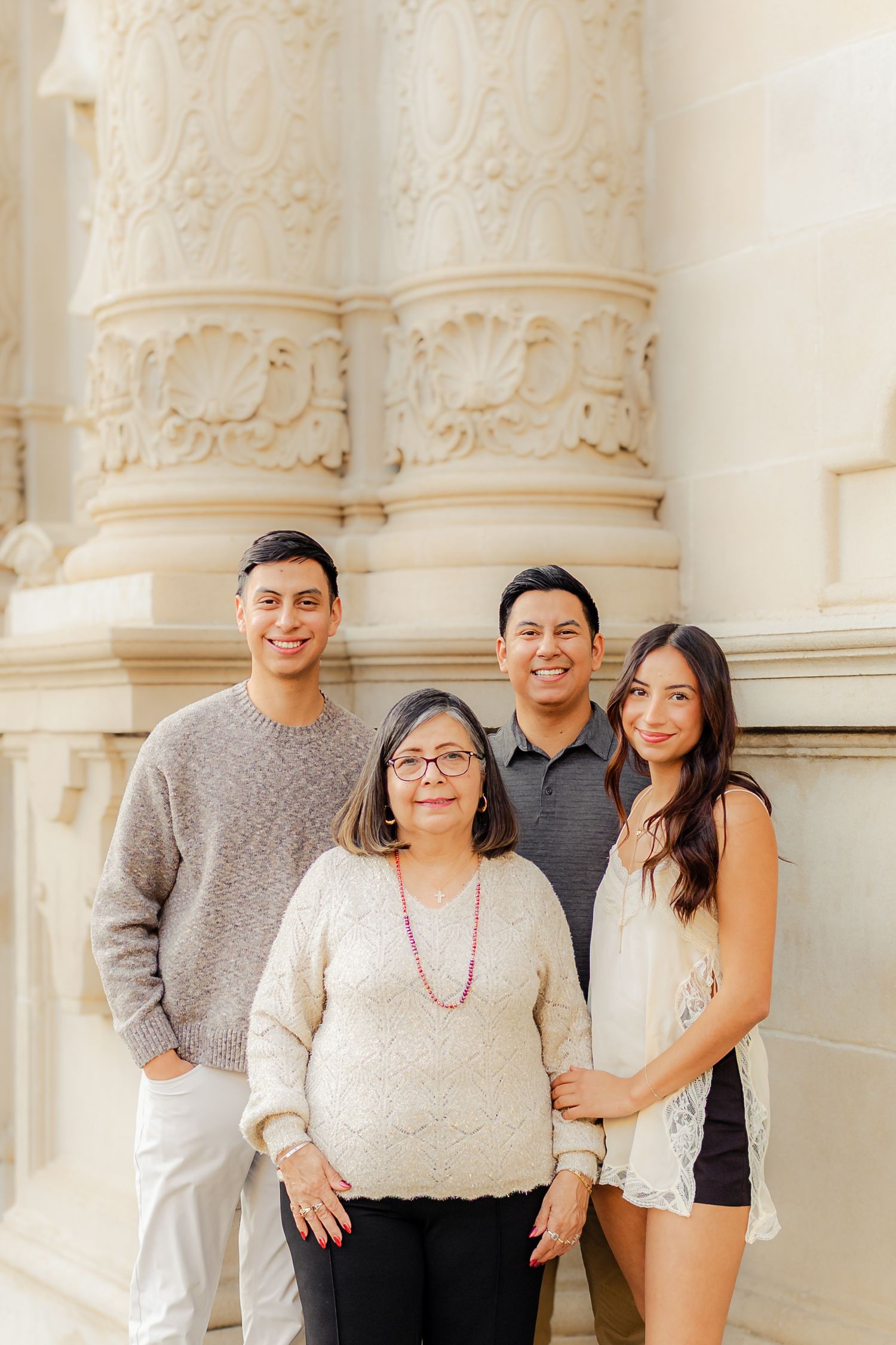 A group poses together in front of decorative architectural columns wearing coordinated neutral-toned outfits.