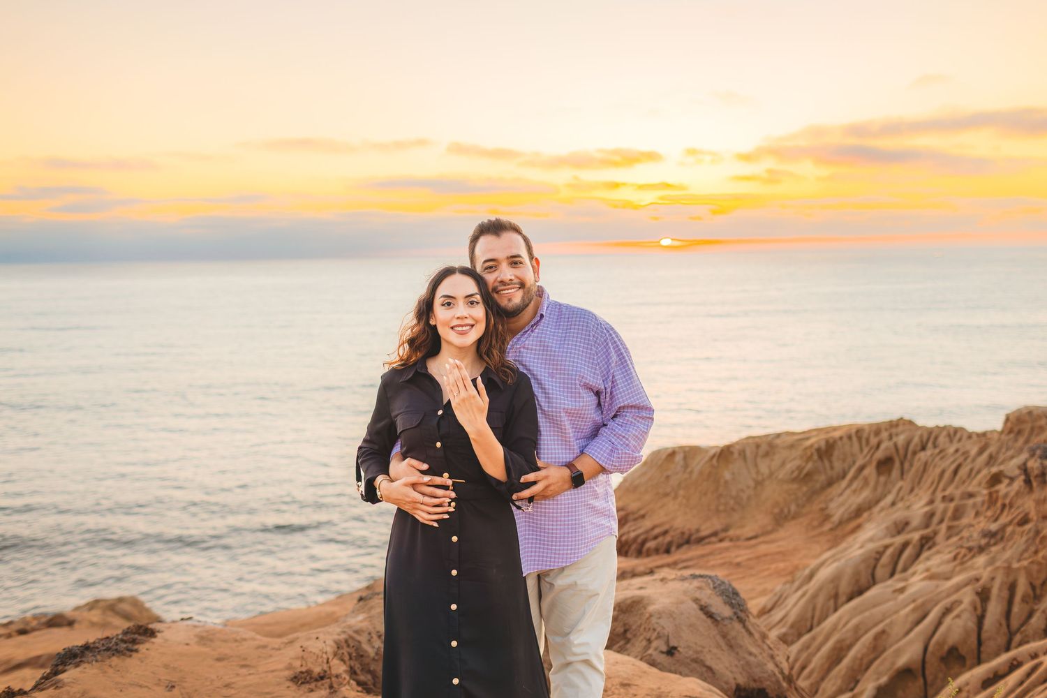 Couple embracing on coastal cliffs during golden hour sunset with ocean views.