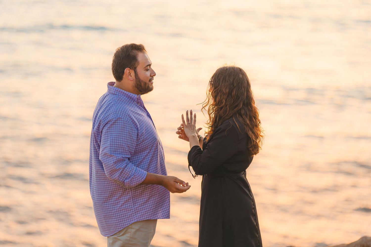 Two people having an emotional conversation at sunset with golden light reflecting off the ocean in the background.