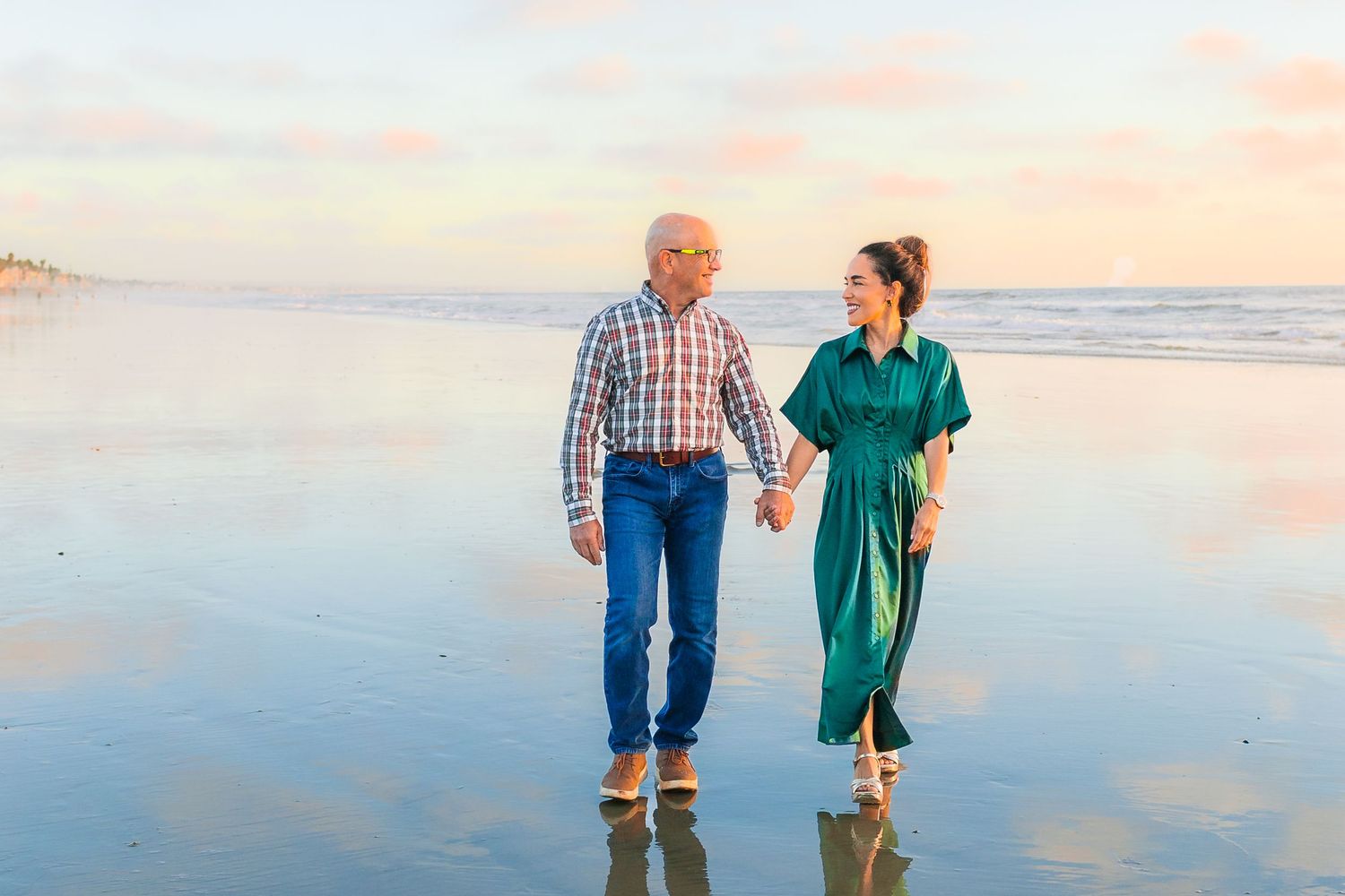 Two people walk hand in hand along a beach at sunset with waves gently rolling onto the shore.