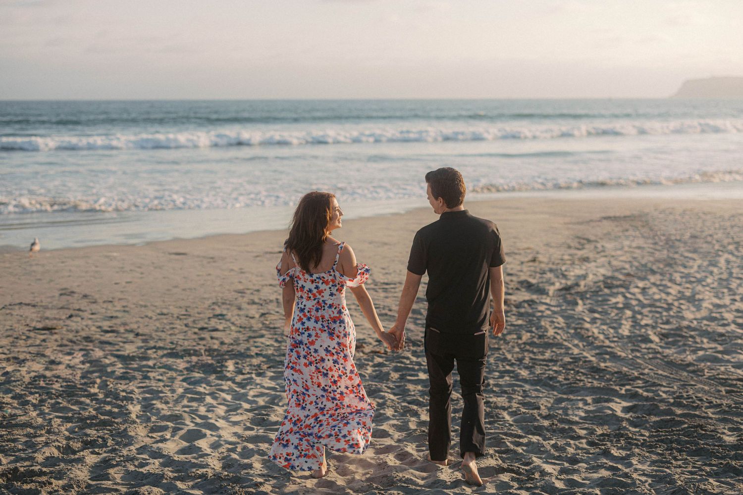 Couple walking hand in hand along the shoreline with Hotel del Coronado in the background.