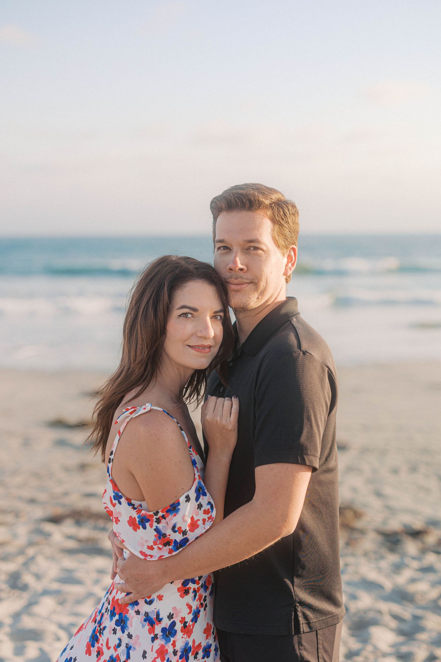 A tender moment shared between a couple on a sunny beach with ocean waves in the background.