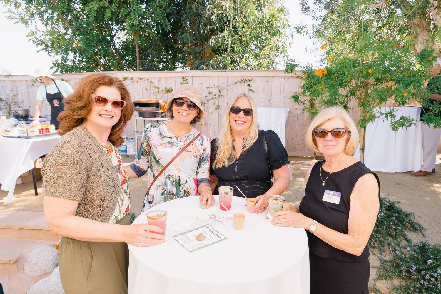 People mingling and socializing at an outdoor garden party under tree shade.