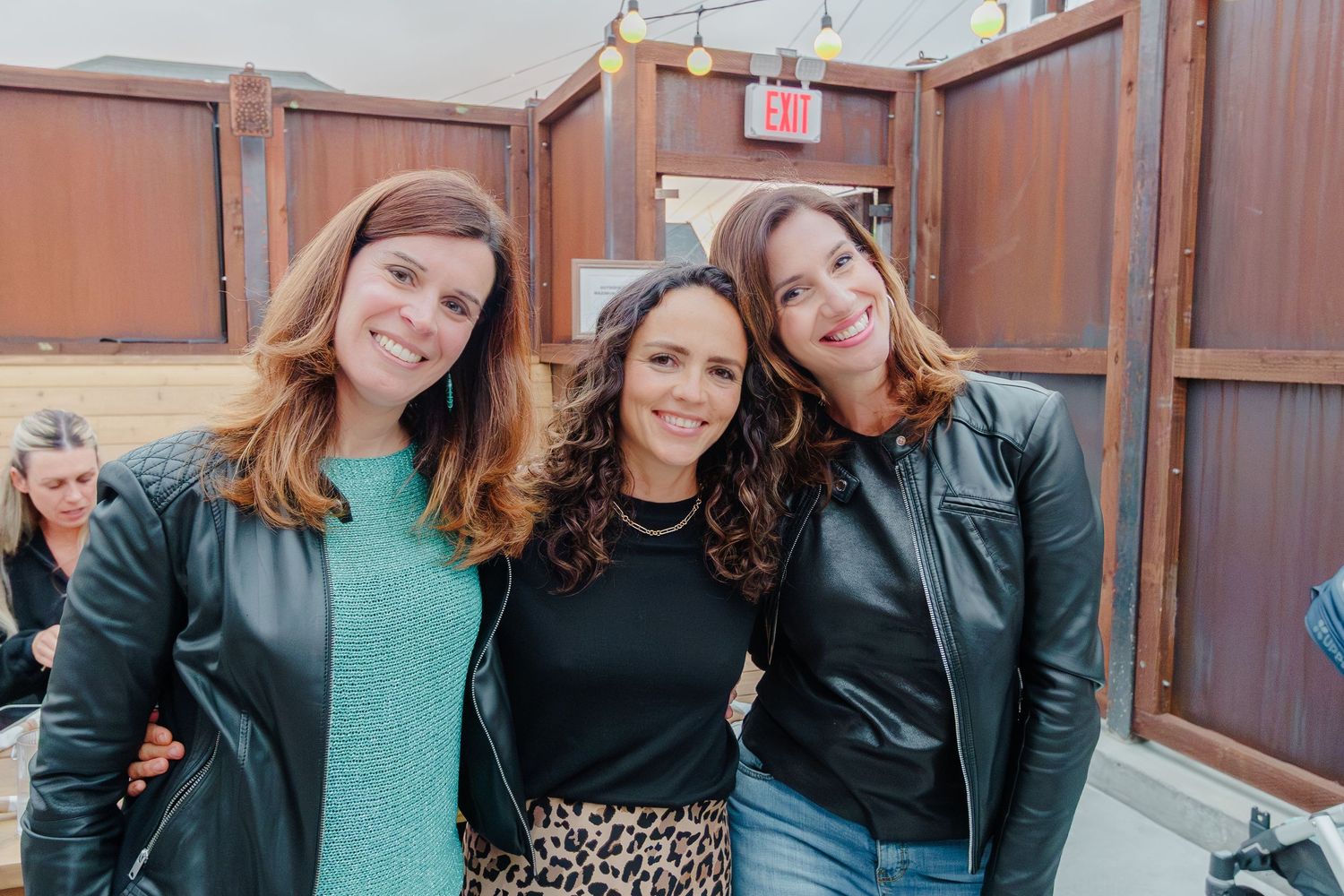 Friends gathered for drinks at an outdoor venue with industrial brick walls and string lights.